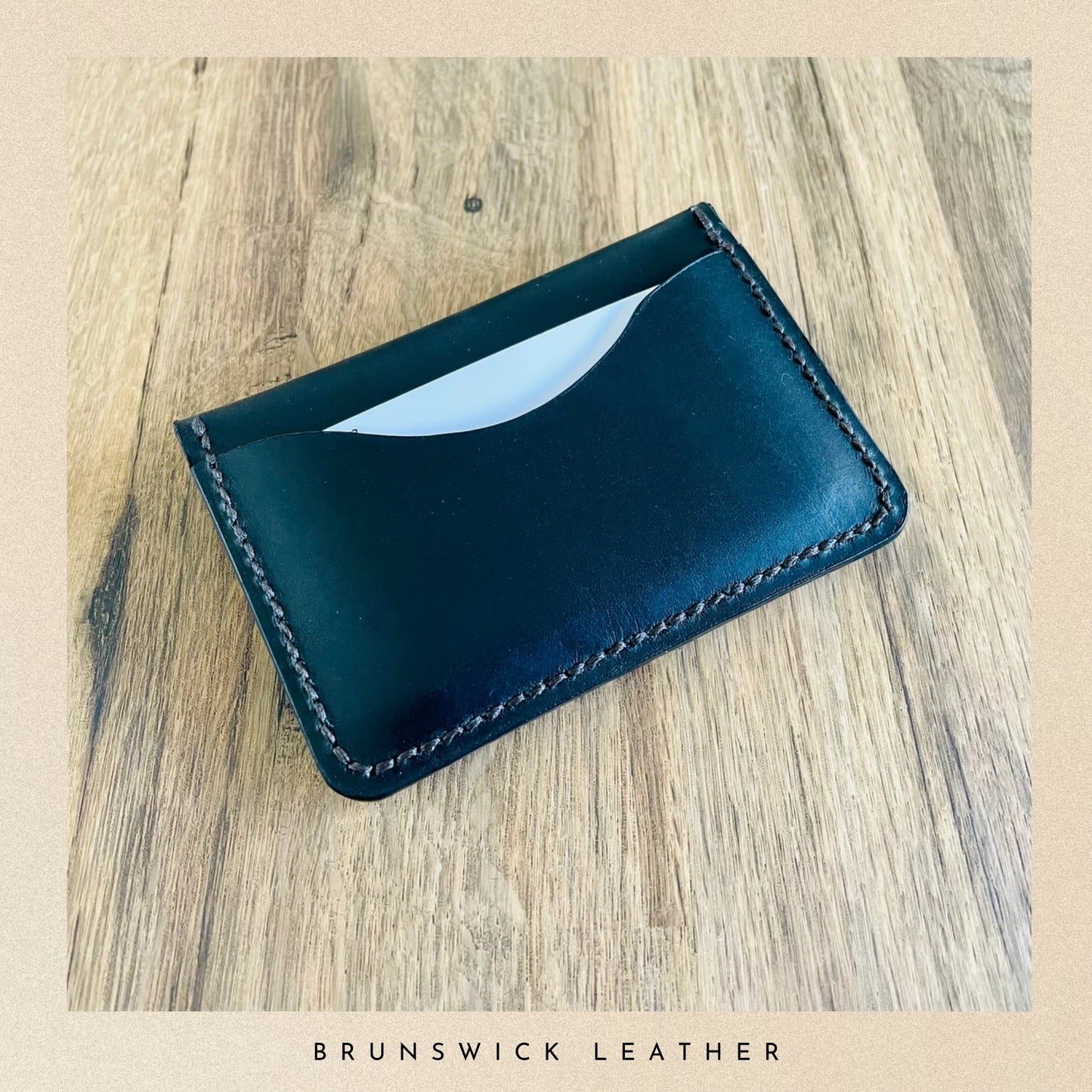 Black leather wallet on a wooden surface with 'Brunswick Leather' branding.