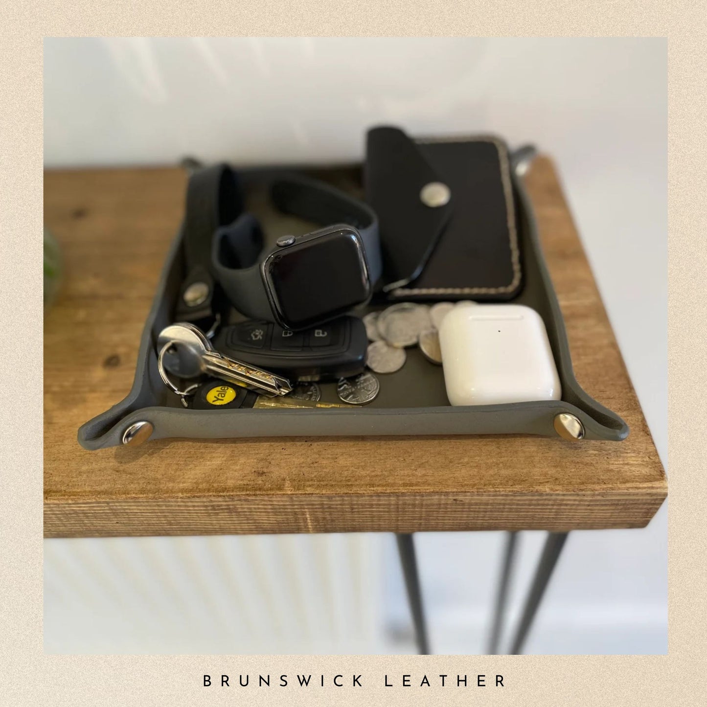 Leather tray with wallet, watch, keys, and coins on a wooden surface with 'Brunswick Leather' branding.
