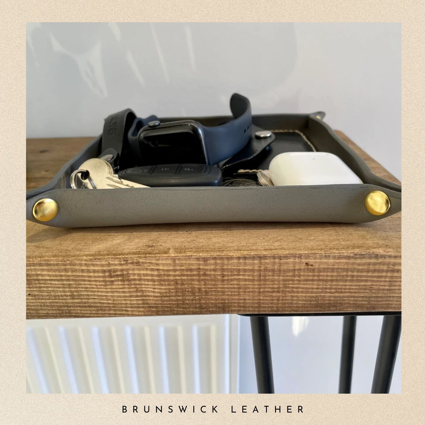 Grey leather tray with gold accents on a wooden surface, featuring a watch and phone.