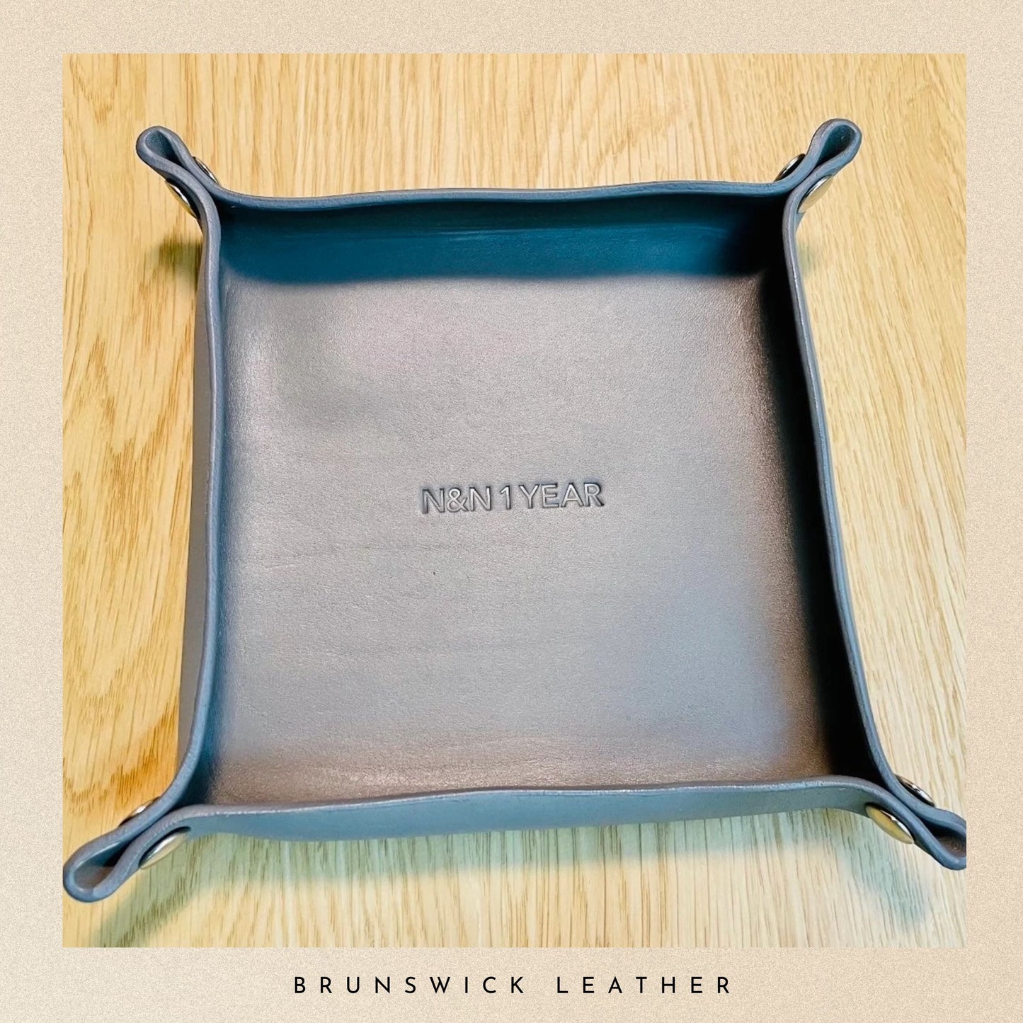 Blue leather tray with 'NHN1YEAR' branding on a wooden surface, featuring 'Brunswick Leather' text.