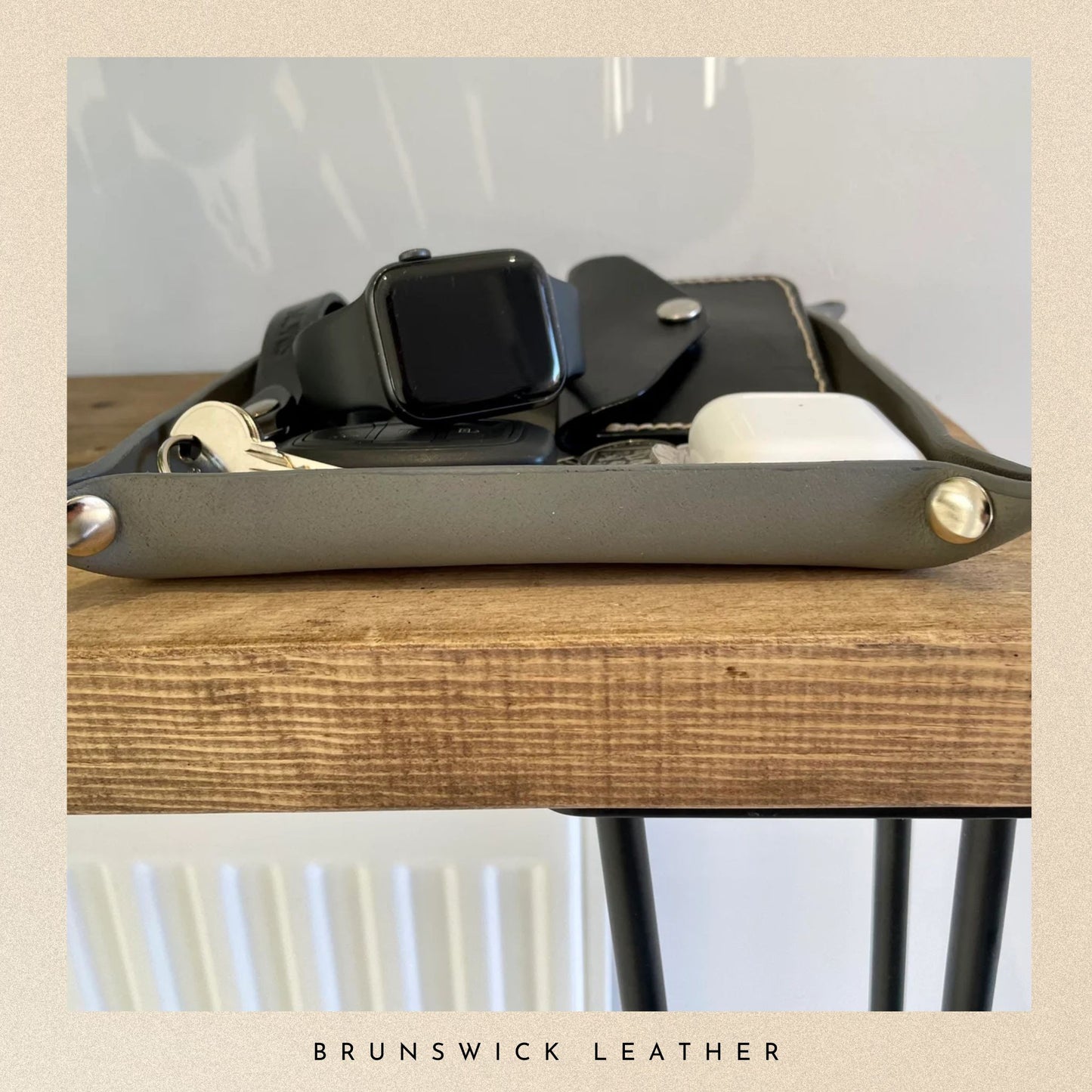 Grey leather tray with a watch on a wooden surface, branded 'Brunswick Leather'.