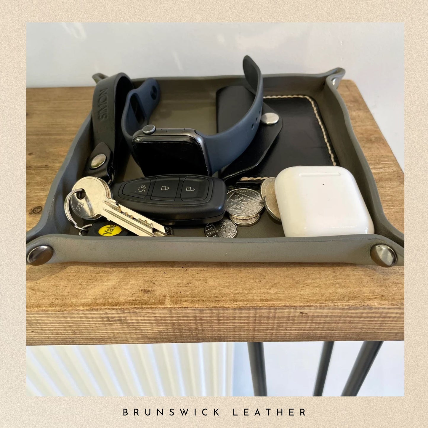 Tray with keys, car remote, coins, and a phone on a wooden surface with 'Brunswick Leather' branding.