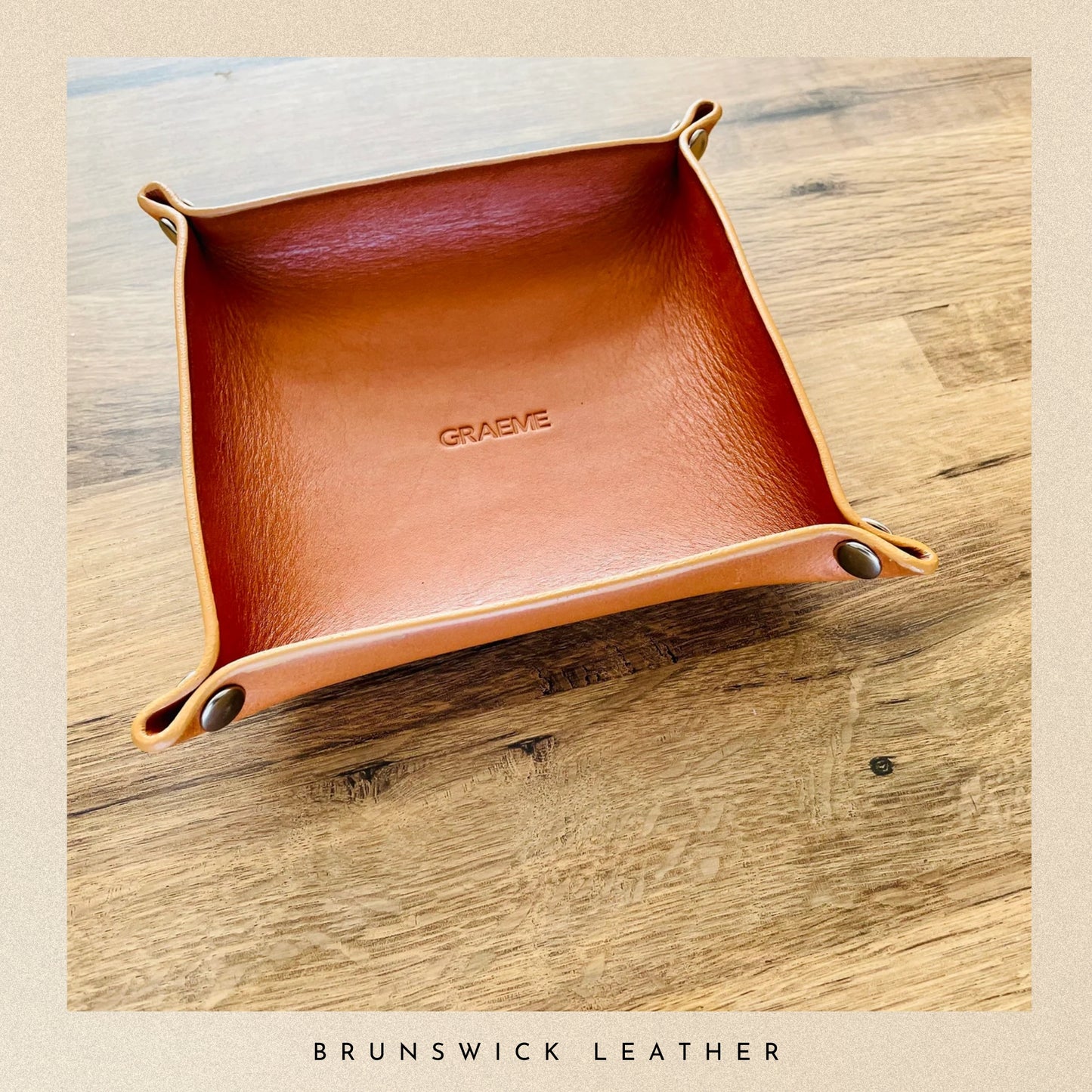 Brown leather tray with 'Brunswick Leather' branding on a wooden surface