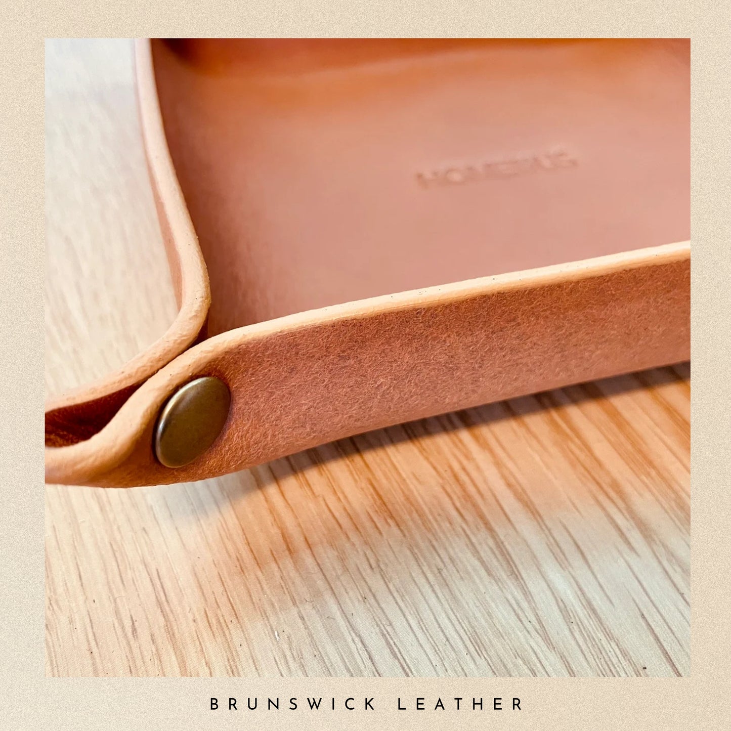 Close-up of a leather tray with branding on a wooden surface, featuring the brand 'Brunswick Leather'.