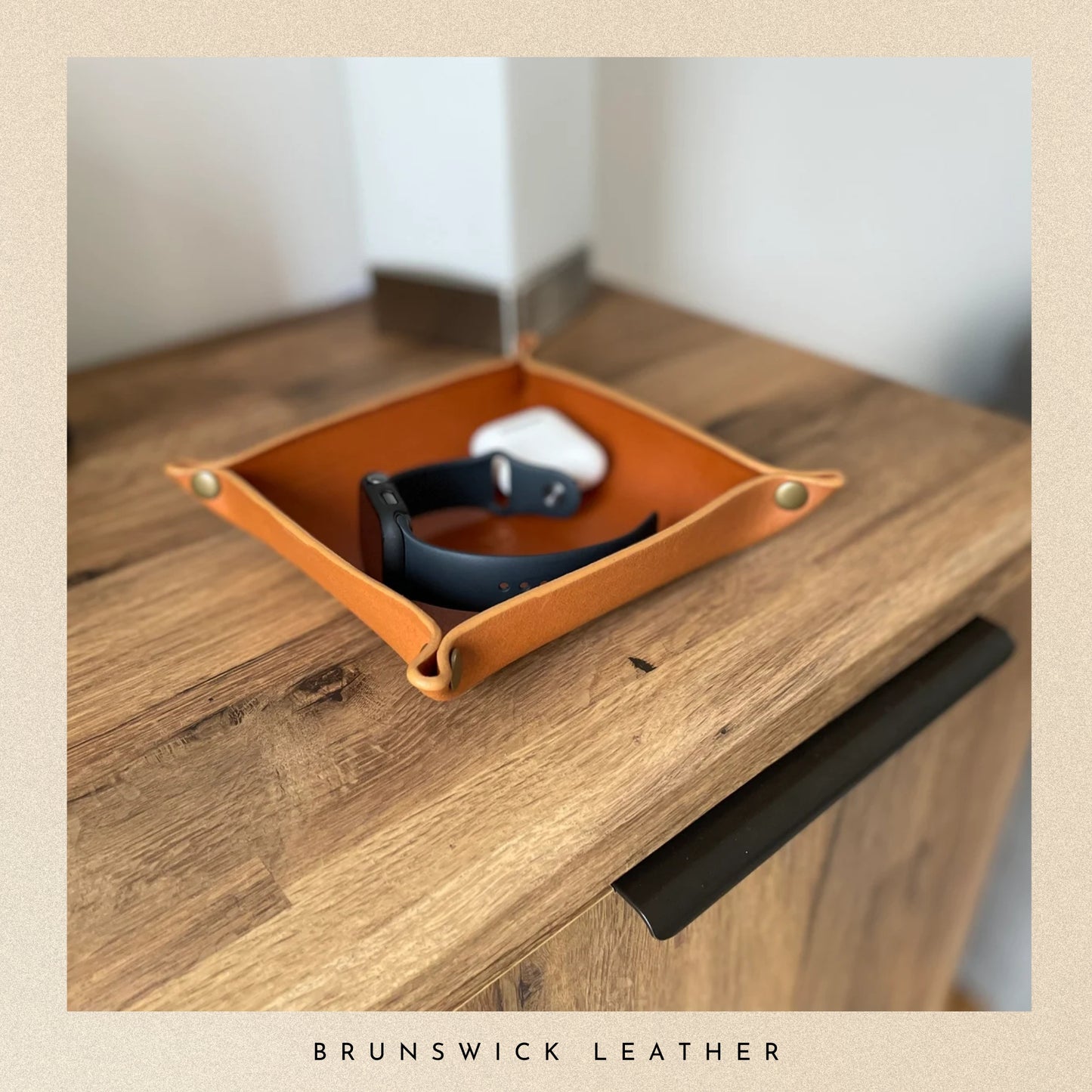 Brown leather tray with a black belt on a wooden surface, branded 'Brunswick Leather'.
