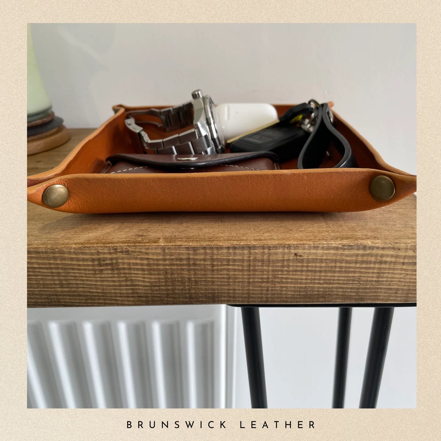 Brown leather tray with accessories on a wooden surface, featuring 'Brunswick Leather' branding.