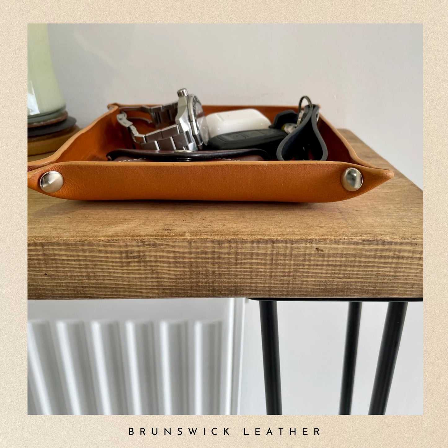 Brown leather tray with metallic accents on a wooden surface, featuring the brand 'Brunswick Leather'.