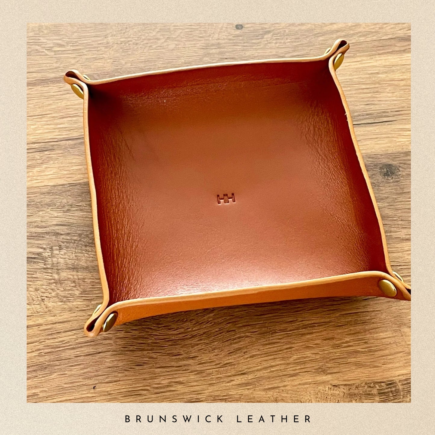 Brown leather tray with gold edges on a wooden surface, branded 'Brunswick Leather'.
