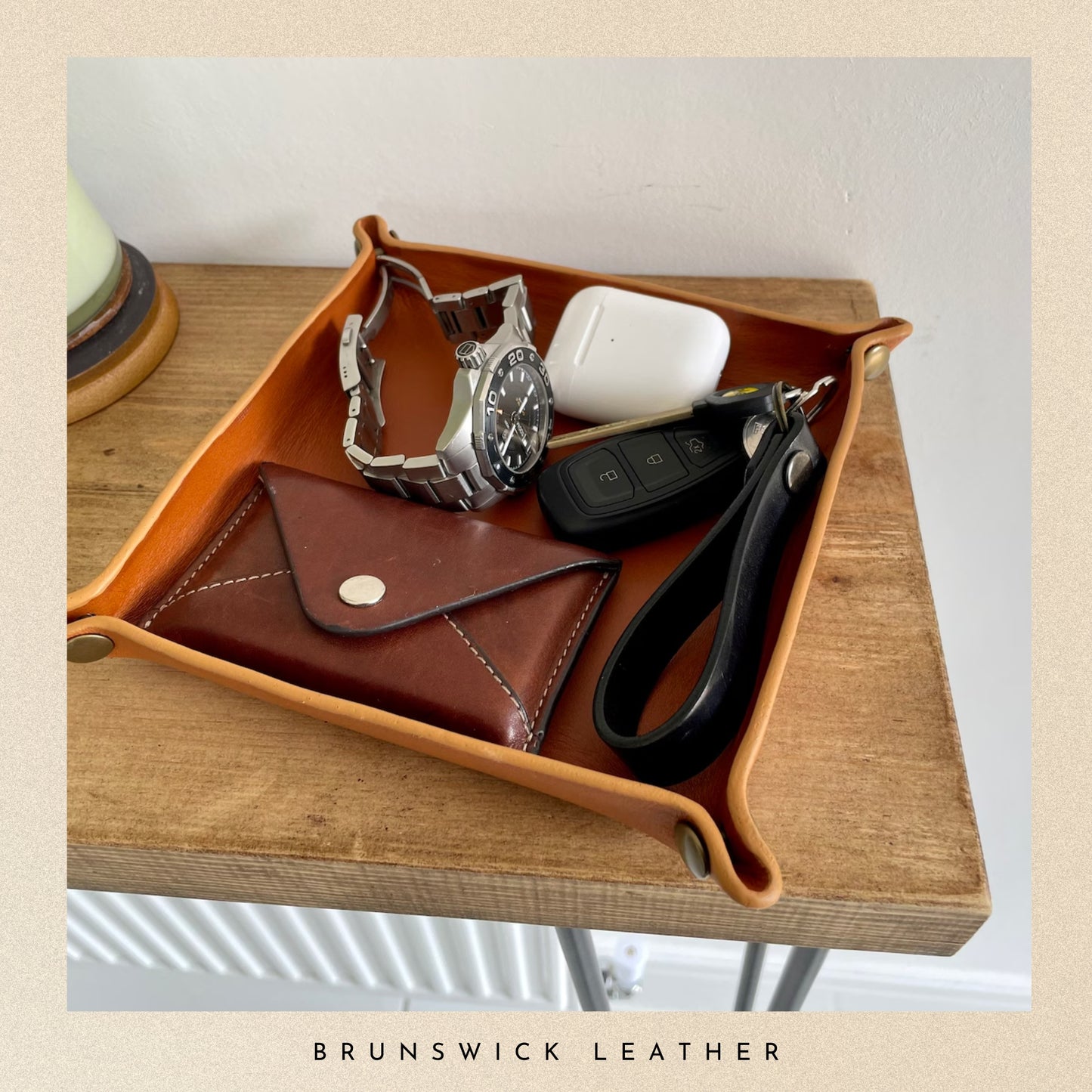 Brown leather tray with accessories on a wooden surface, branded 'Brunswick Leather'.