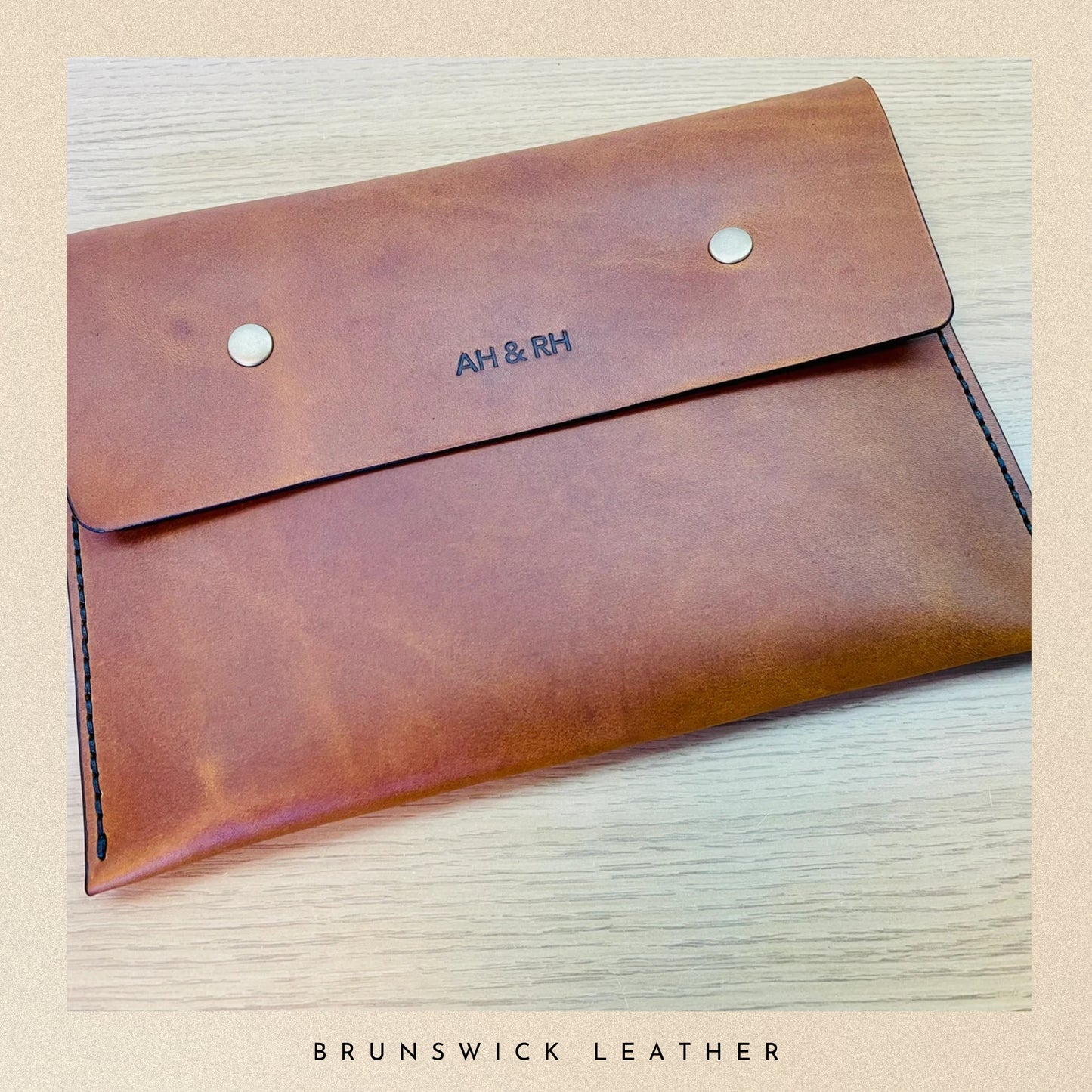 Brown leather envelope with 'AH & RH' branding on a light wood surface, featuring 'Brunswick Leather' text.