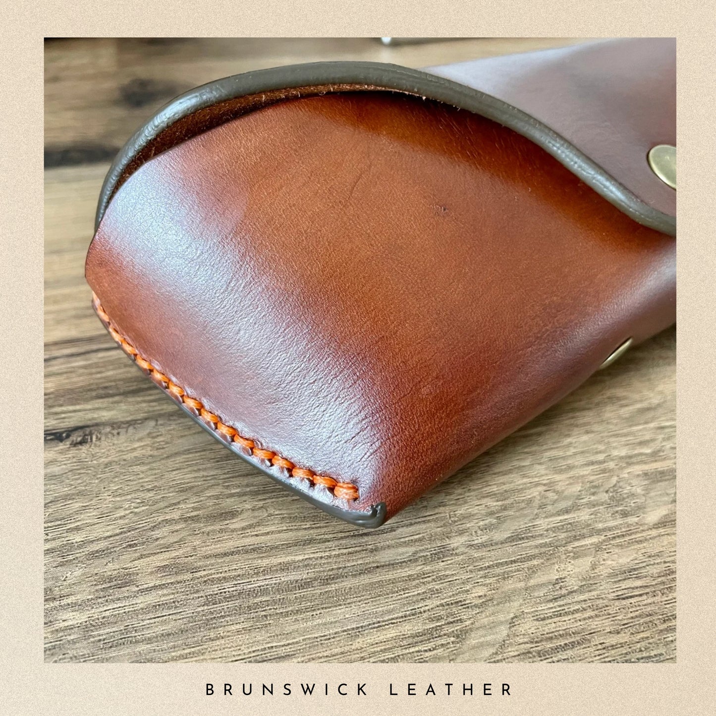 Close-up of a brown leather case with visible stitching on a wooden surface, branded 'Brunswick Leather'.