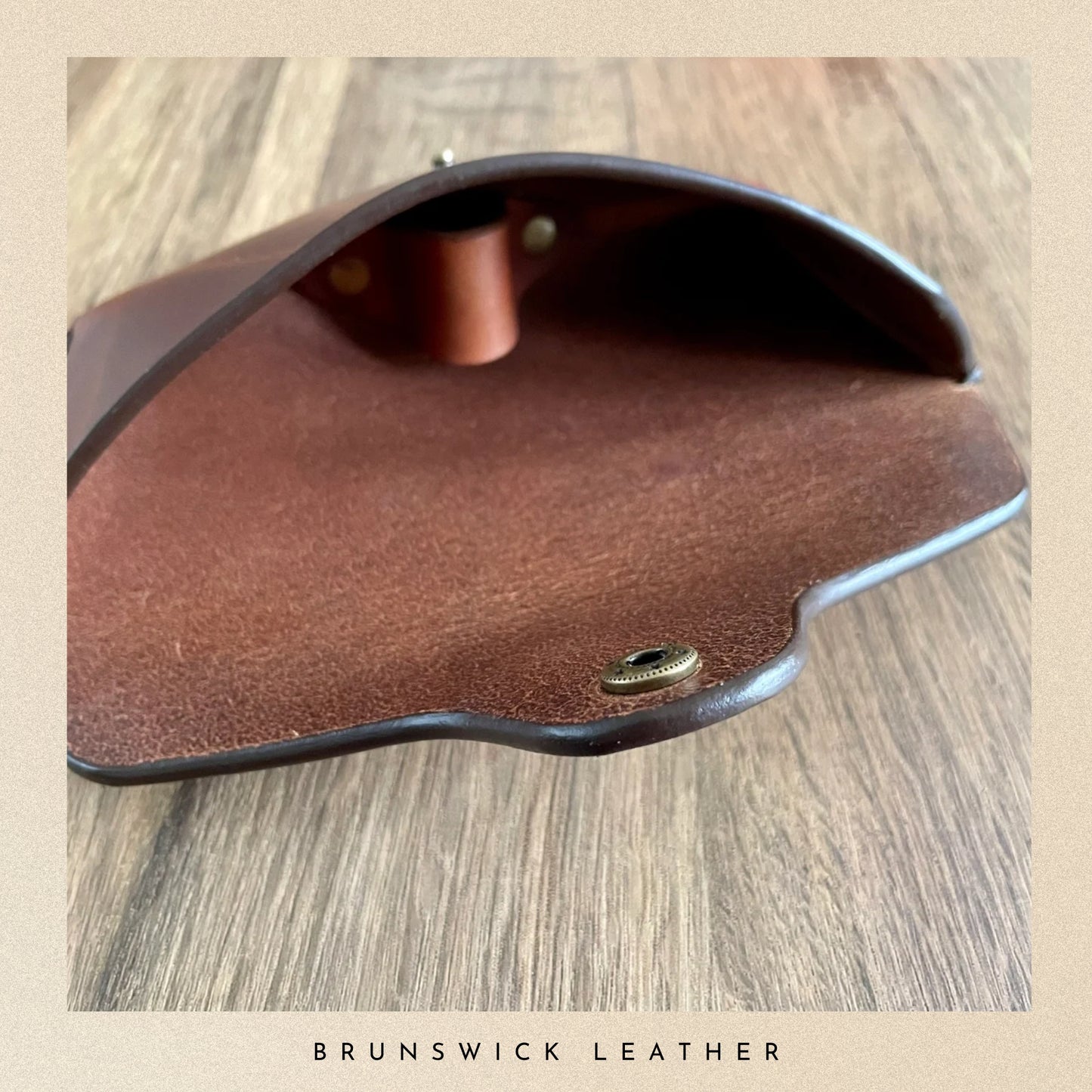 Brown leather case with gold accents on a wooden surface, branded 'Brunswick Leather'.