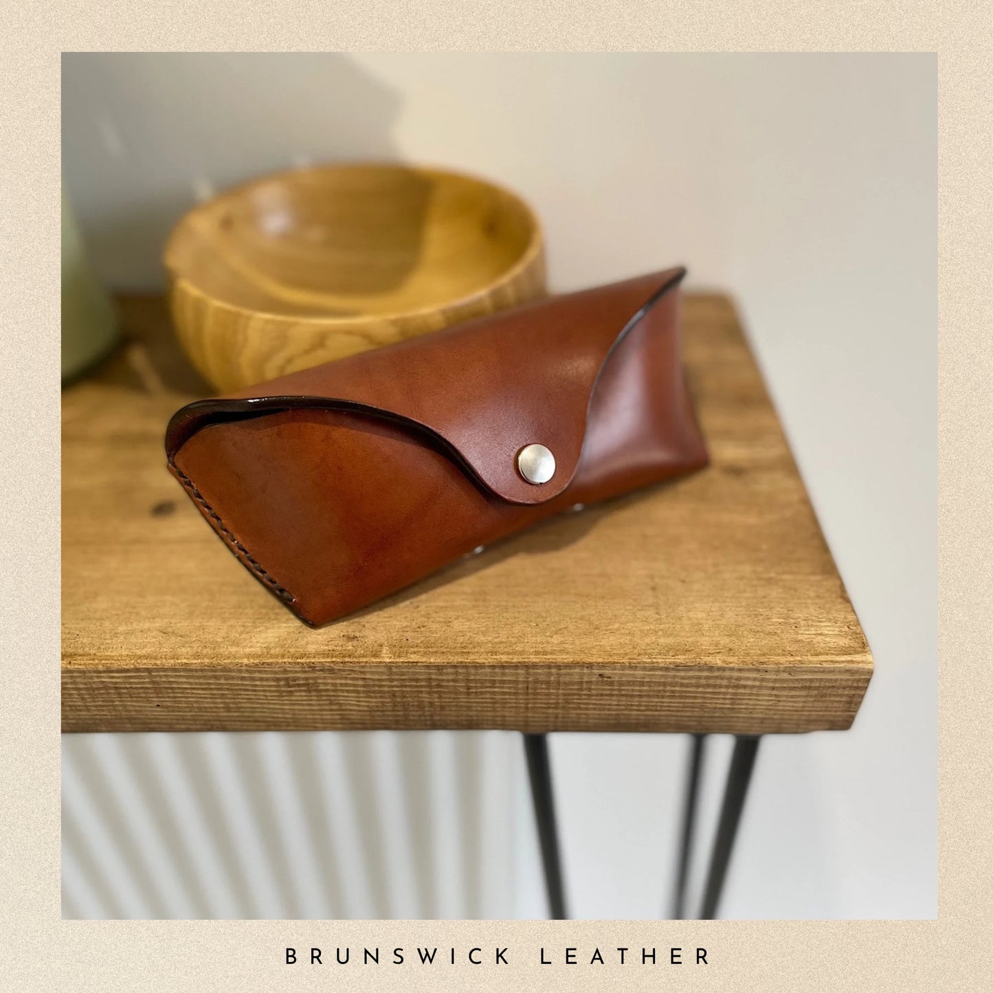 Brown leather pouch with a white button on a wooden surface, branded 'Brunswick Leather'.