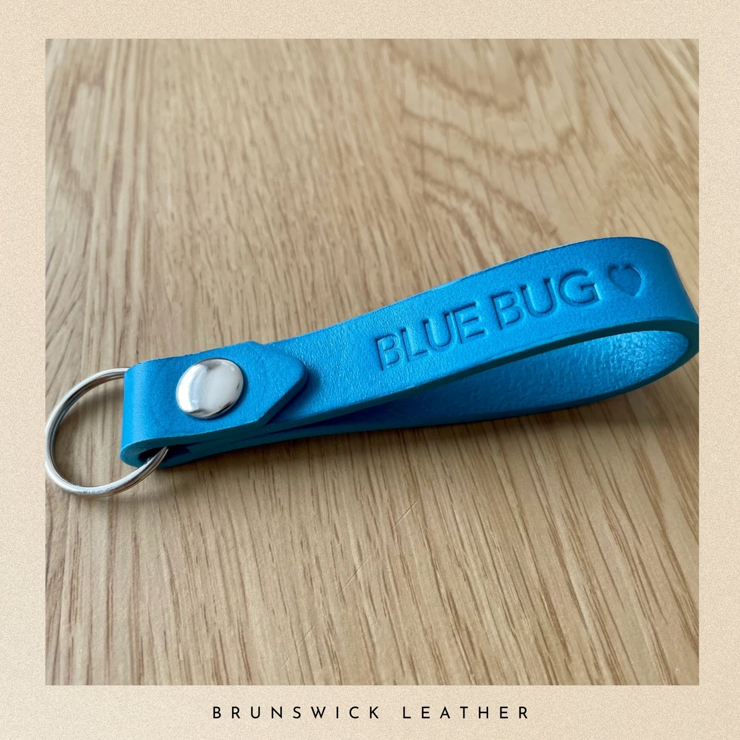 Blue keychain with 'BLUE BUG' text on a wooden surface, branded as Brunswick Leather.