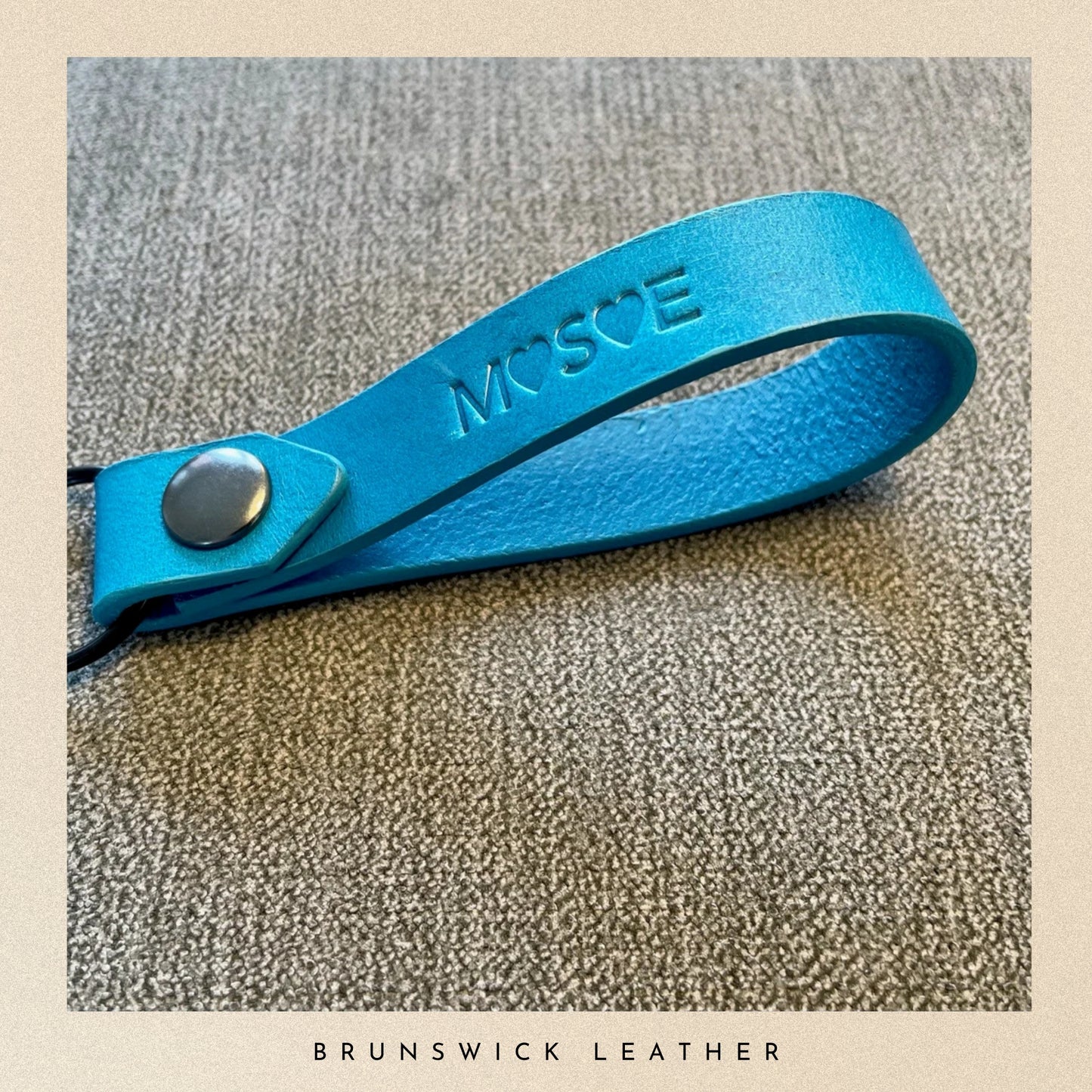 Blue leather strap with a metal buckle on a textured surface, branded 'Mose'.