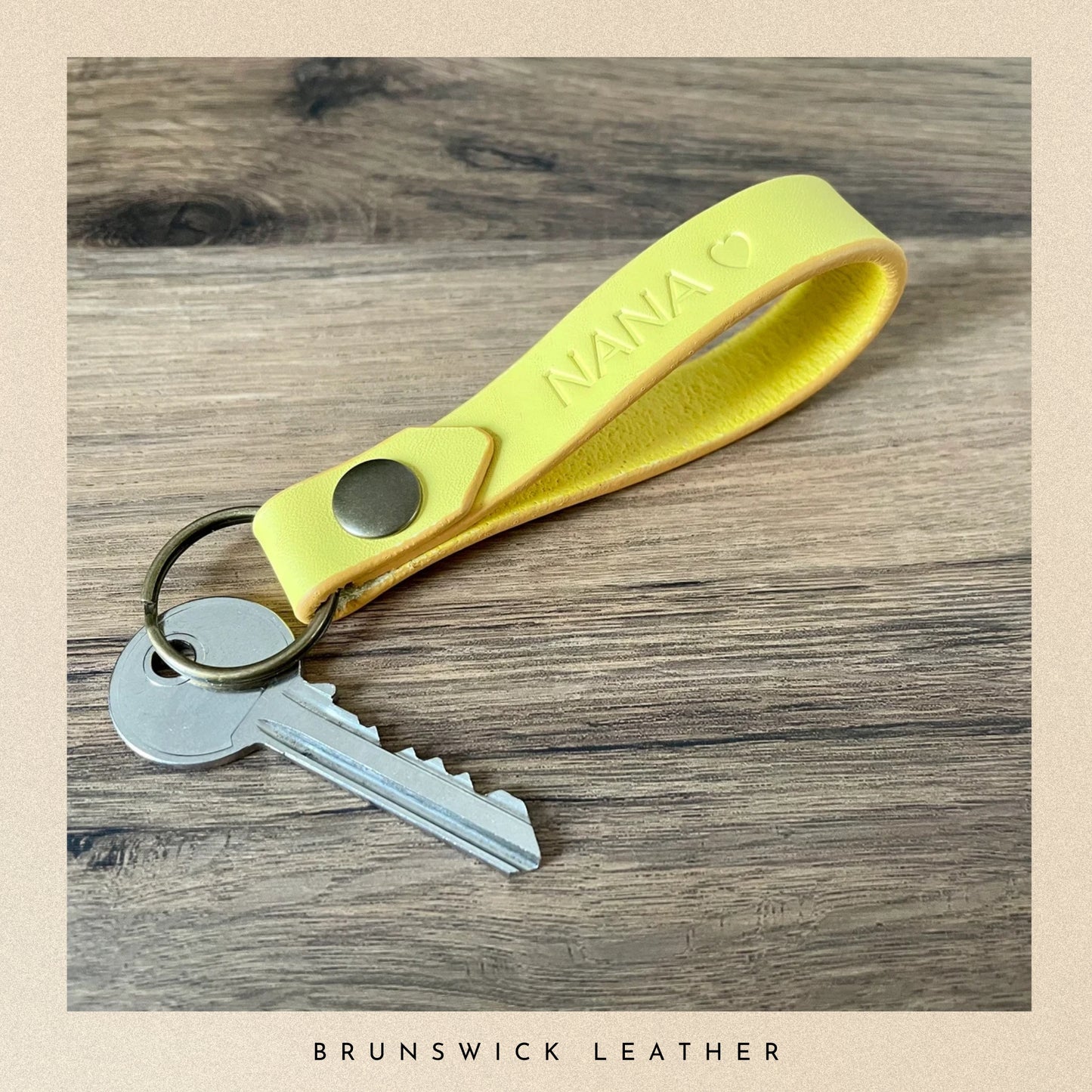 Yellow keychain with a key on a wooden surface, branded 'Nana'.