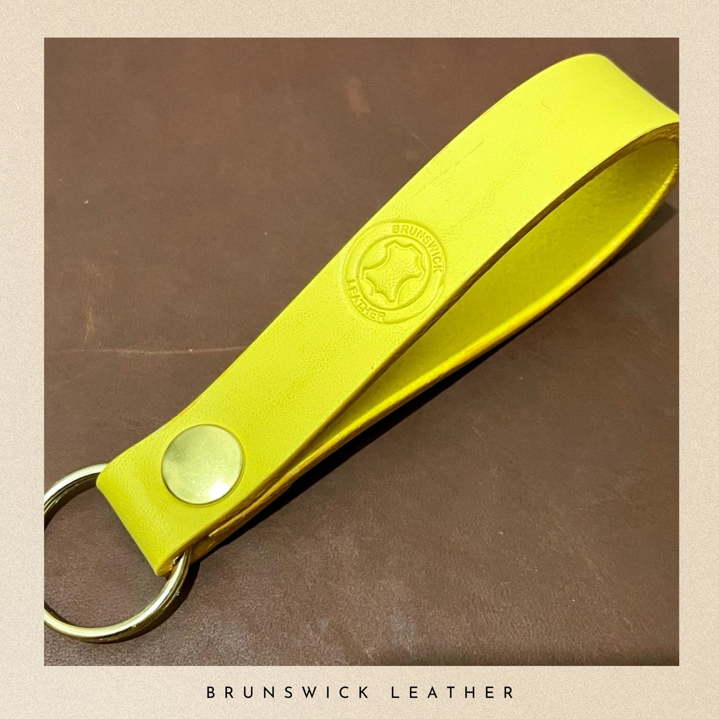 Yellow leather keychain with a brand logo on a brown background