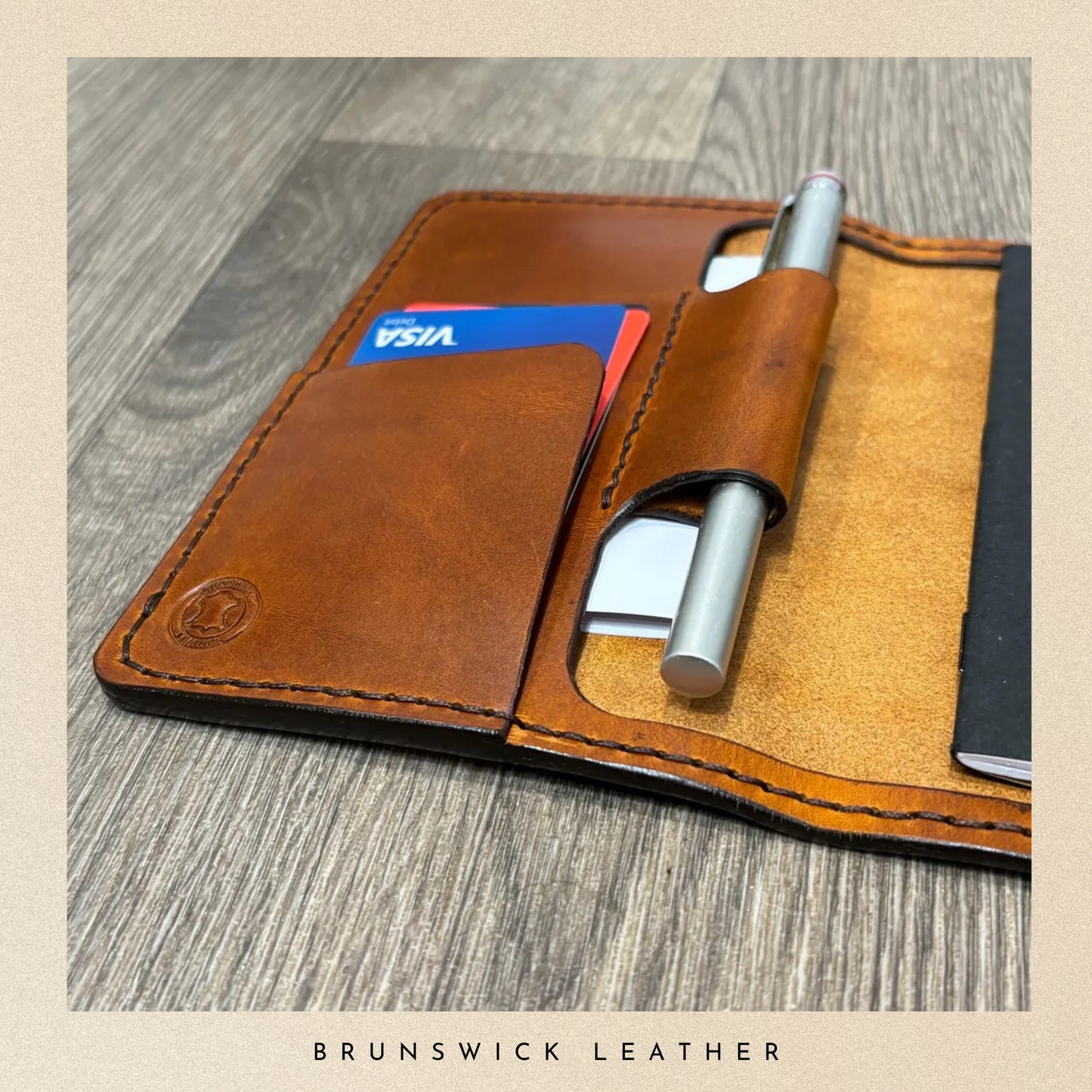 Brown leather wallet with card slots and pen holder on a wooden surface, branded 'Brunswick Leather'.