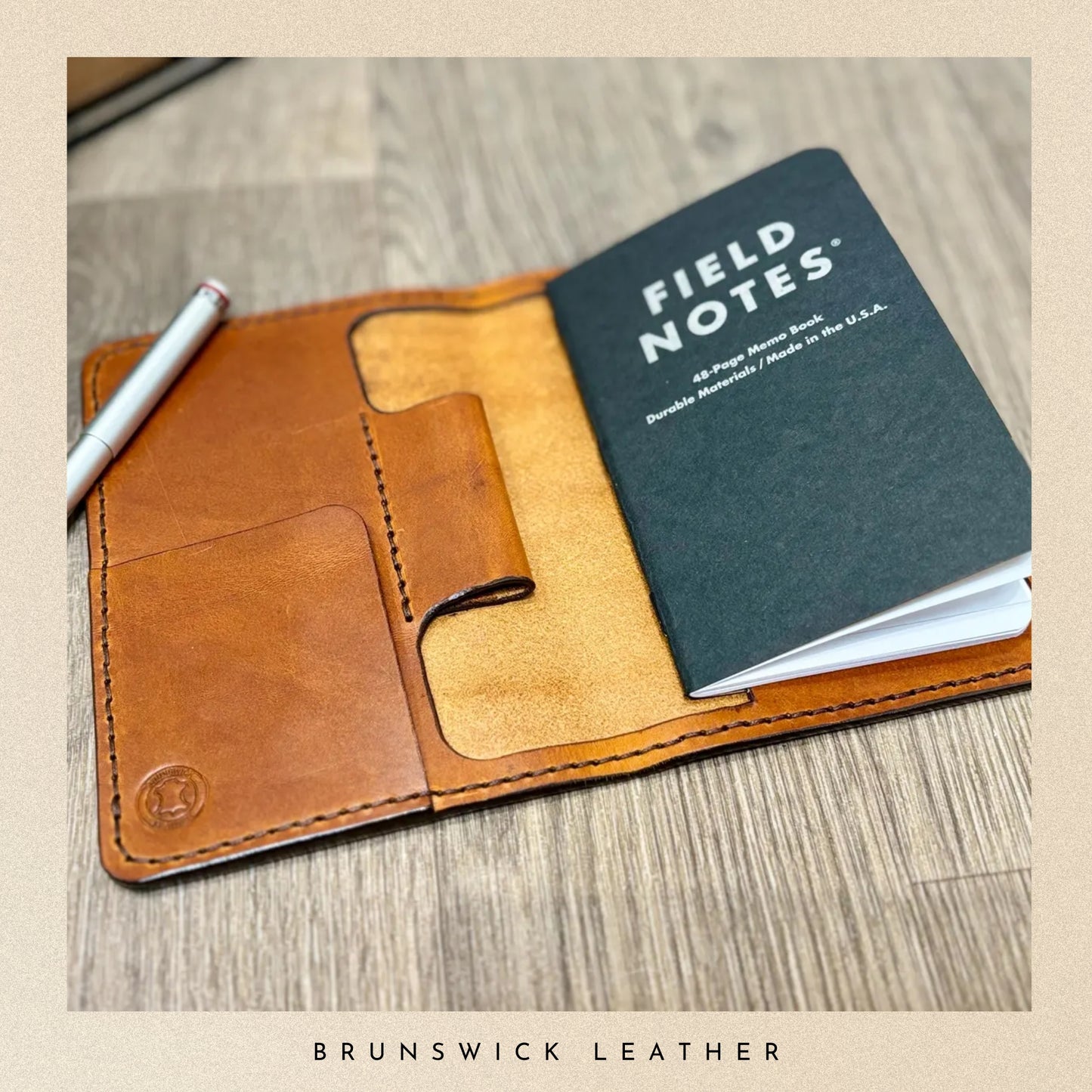 Brown leather notebook cover with a Field Notes notebook and pen on a wooden surface, branded 'Brunswick Leather'.