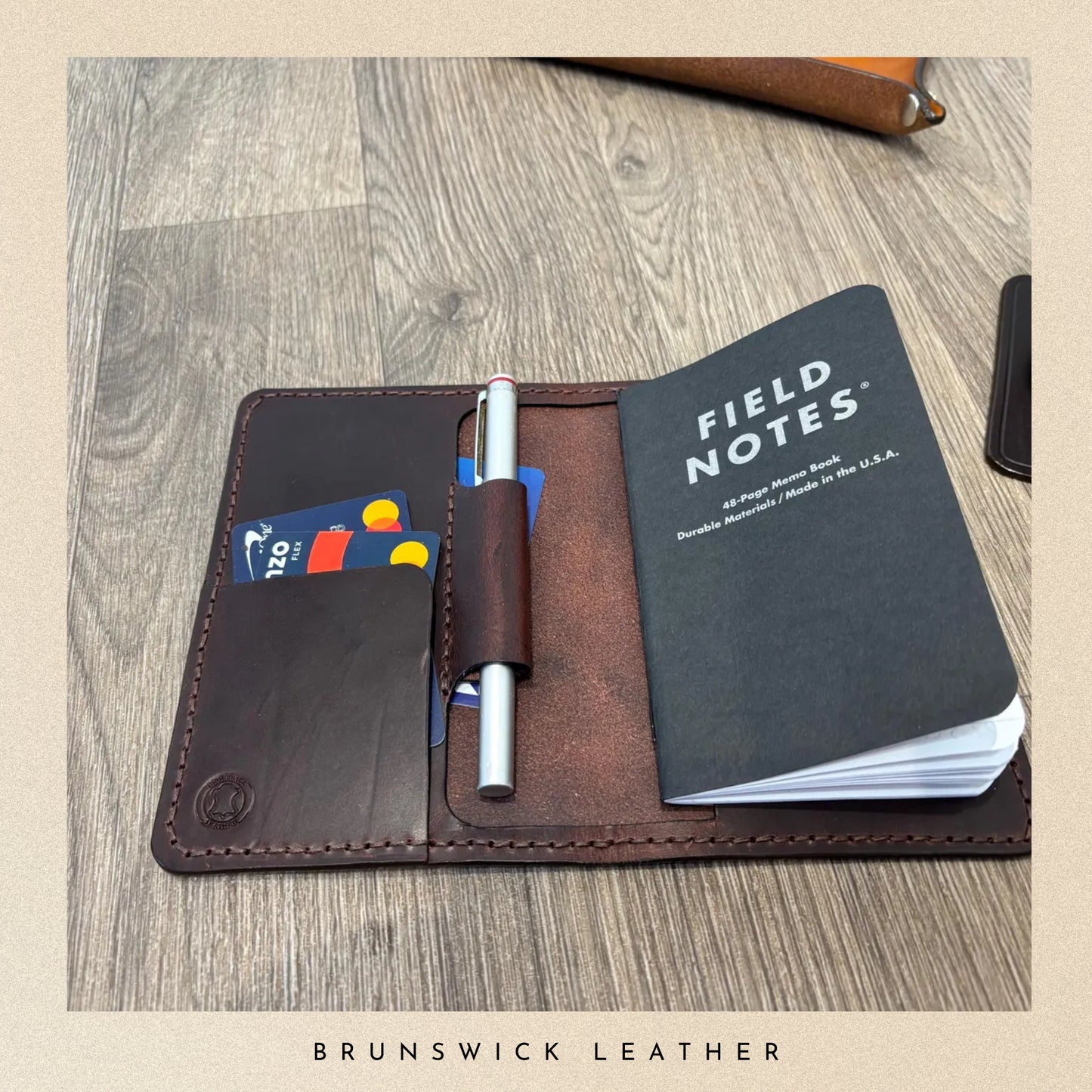 Brown leather wallet with a Field Notes notebook and cards on a wooden surface, branded 'Brunswick Leather'.