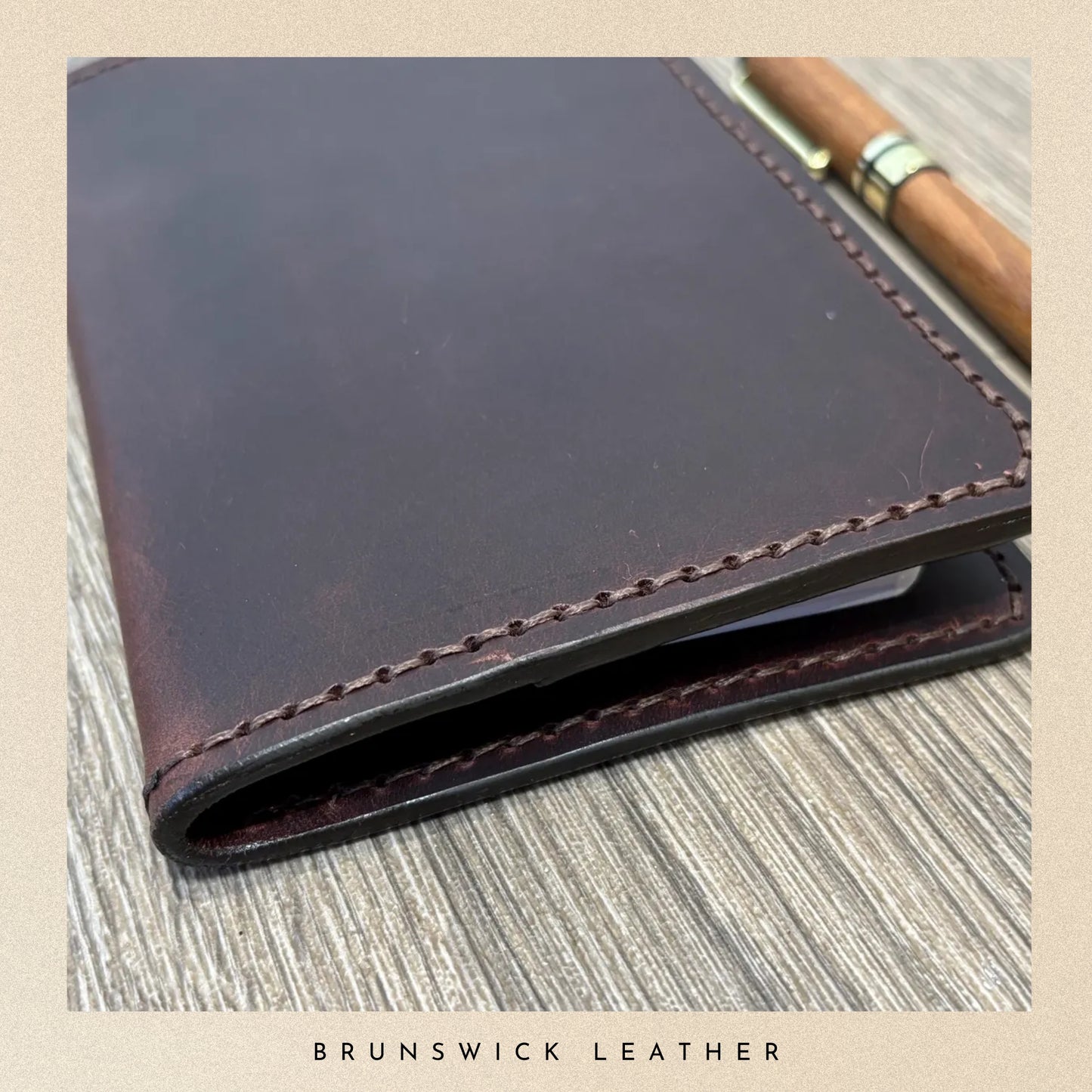 Brown leather notebook with pen on a textured surface, branded 'Brunswick Leather'.