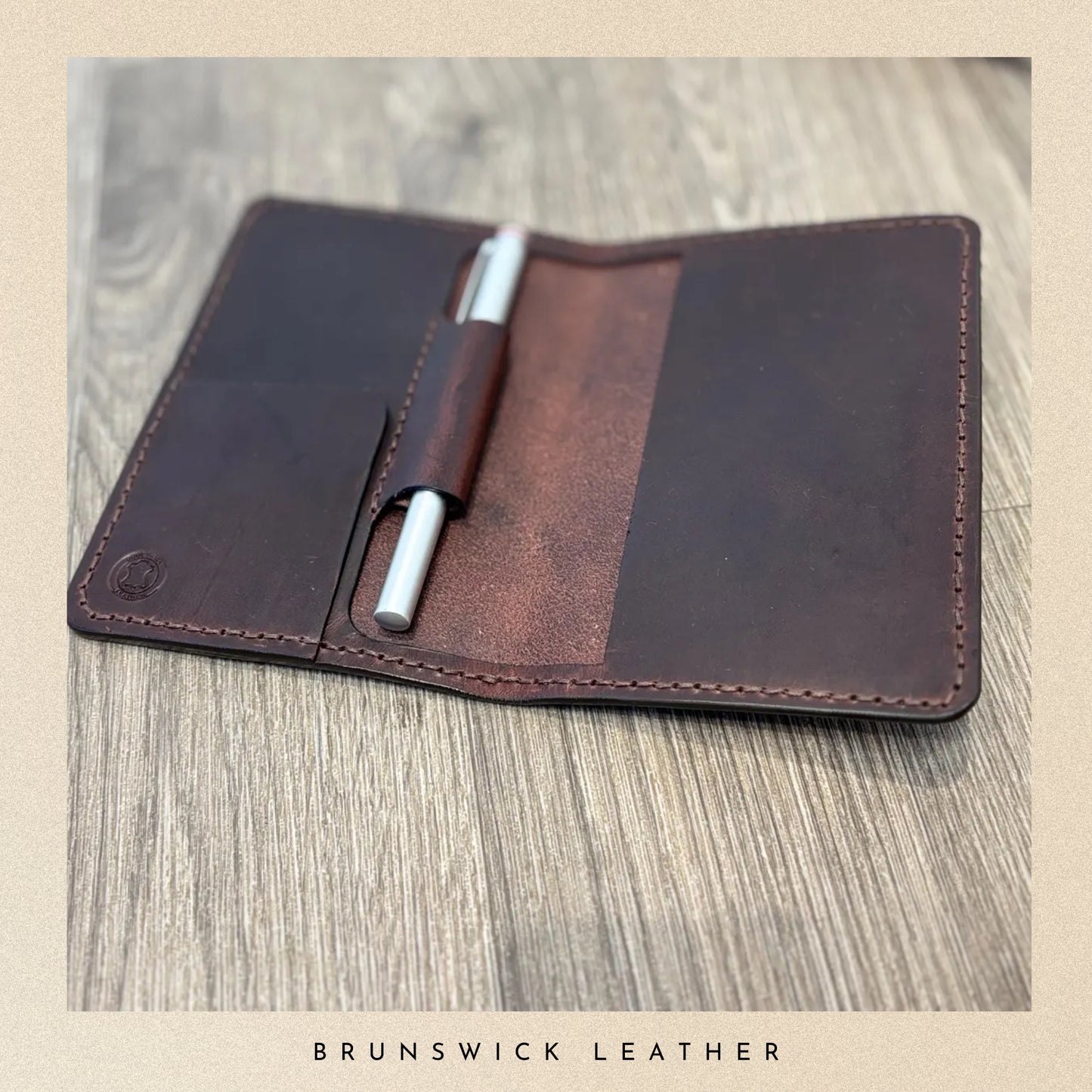 Brown leather notebook cover with a pen on a wooden surface, branded 'Brunswick Leather'.