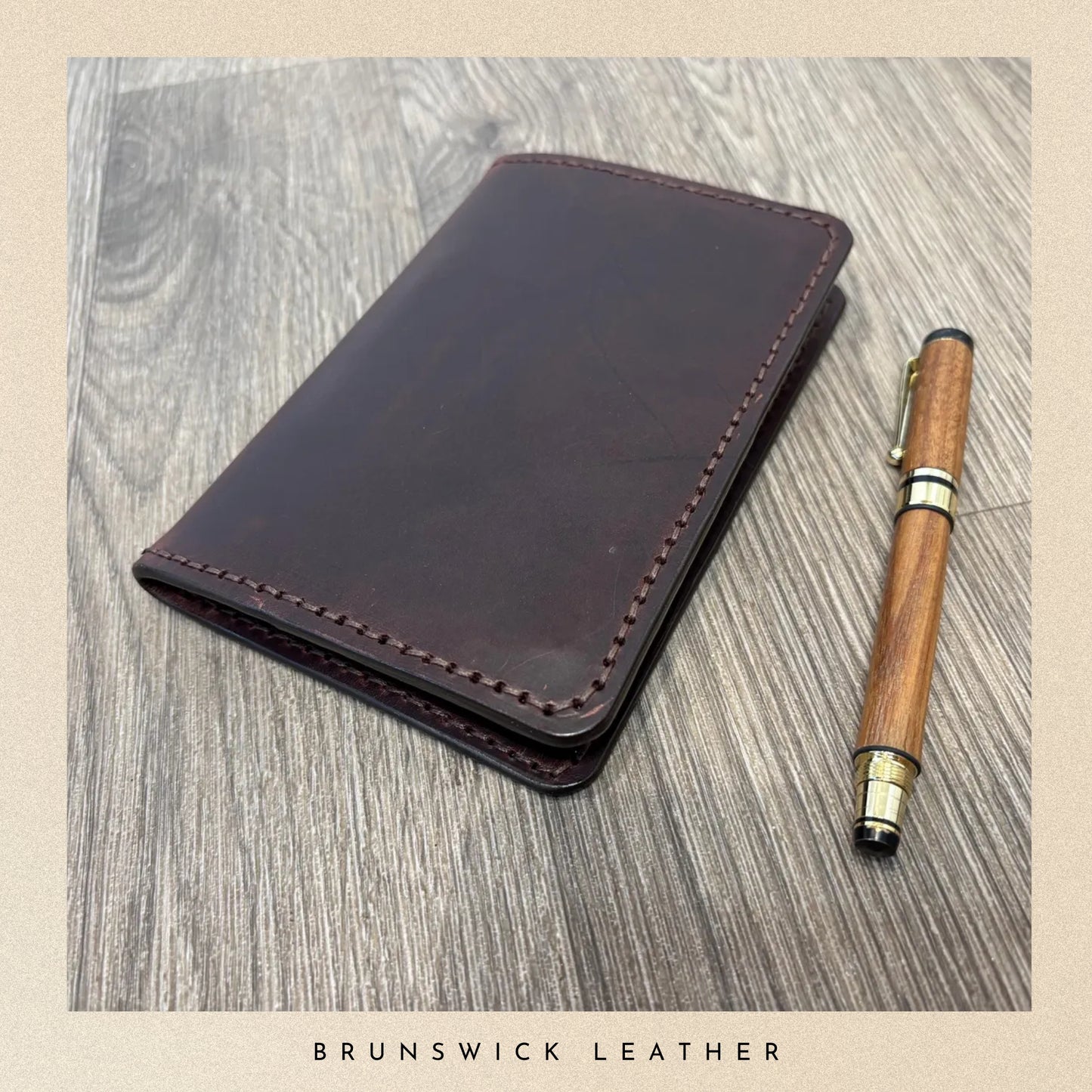 Brown leather wallet and wooden pen on a wooden surface with 'Brunswick Leather' branding.