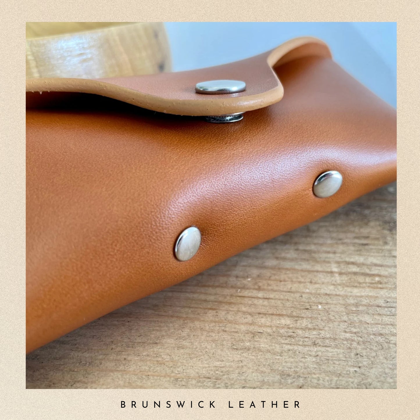 Close-up of a brown leather product with metal studs on a wooden surface, branded 'Brunswick Leather'.