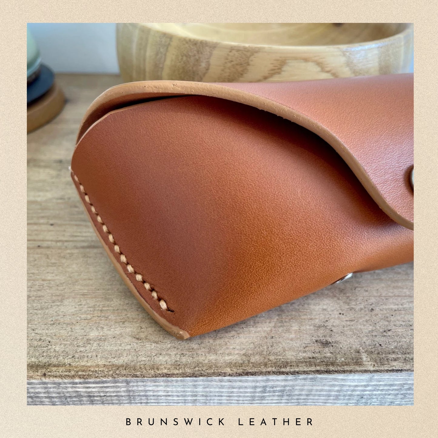Close-up of a brown leather product with visible stitching on a wooden surface, branded 'Brunswick Leather'.