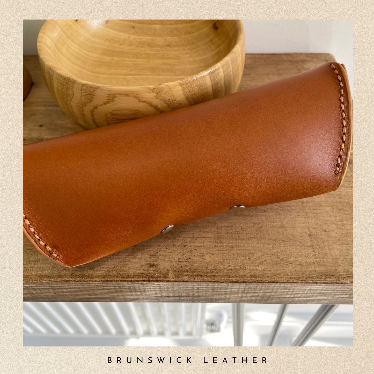 Brown leather case on a wooden surface with 'Brunswick Leather' branding.