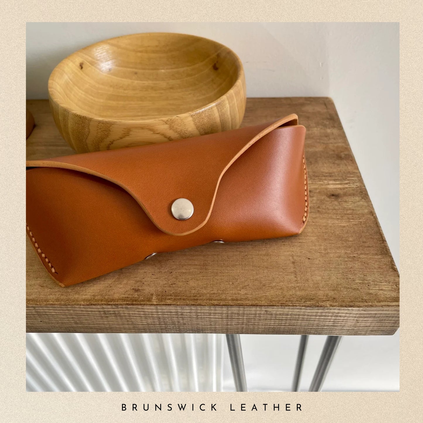 Brown leather pouch with silver button on a wooden surface, branded 'Brunswick Leather'.