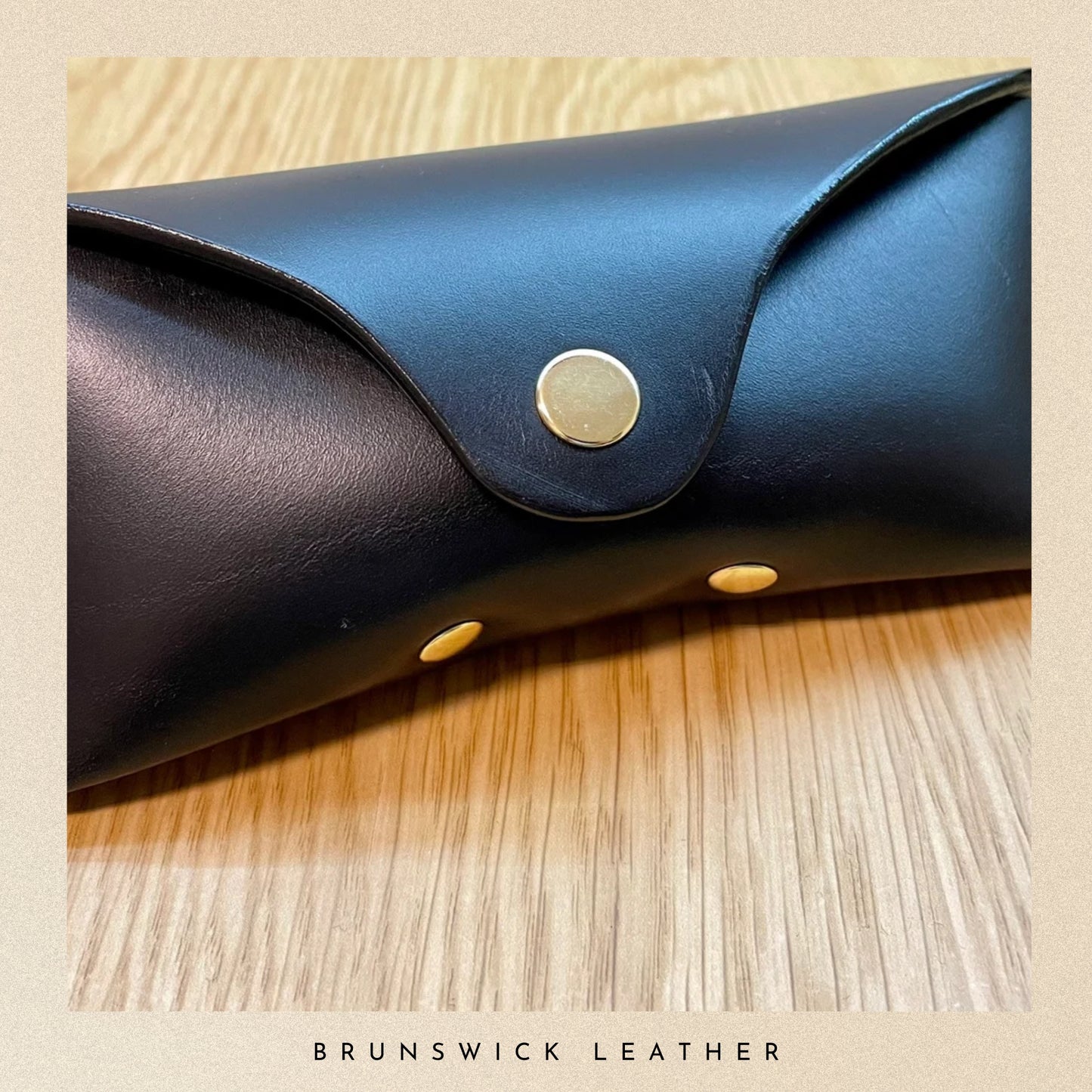 Blue leather case with gold studs on a wooden surface, branded 'Brunswick Leather'.