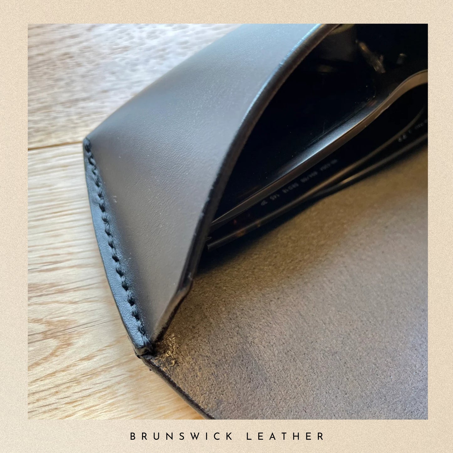 Close-up of a black leather wallet on a wooden surface with 'Brunswick Leather' branding.