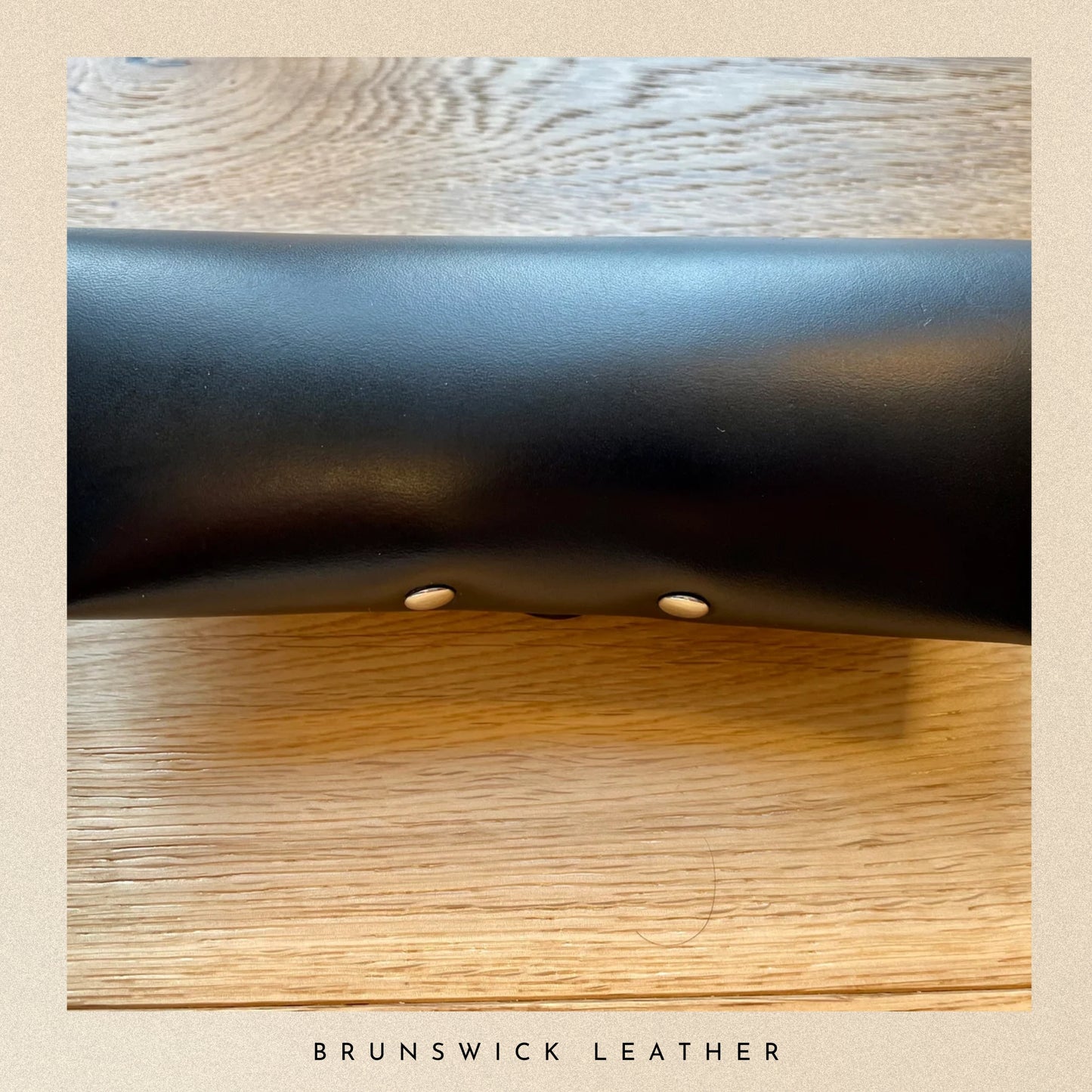Close-up of black leather surface on a wooden background with 'Brunswick Leather' branding.