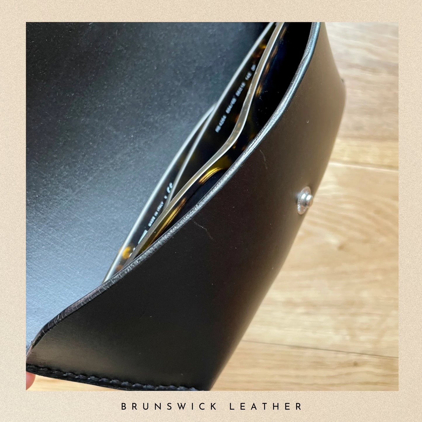 Close-up of a black leather product with gold accents on a wooden surface, branded 'Brunswick Leather'.