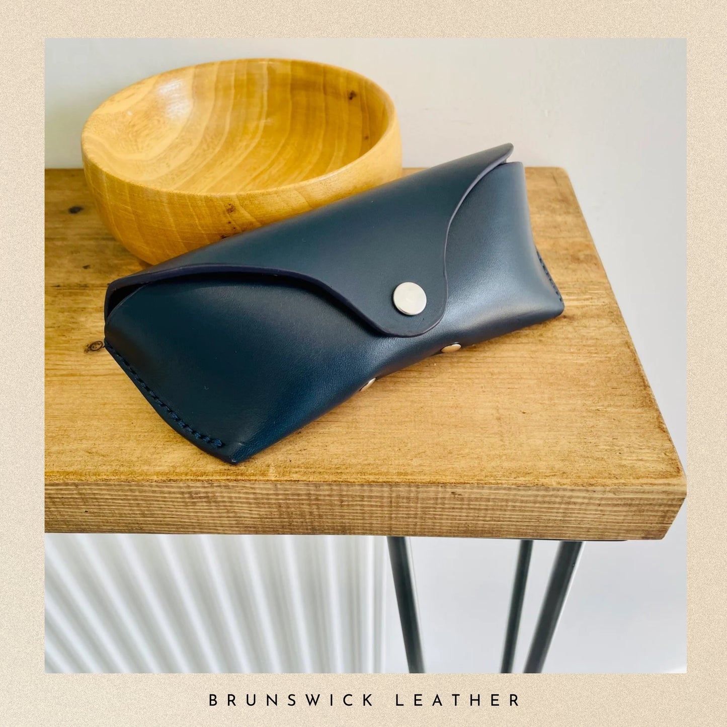 Black leather pouch with a button on a wooden surface, branded 'Brunswick Leather'.
