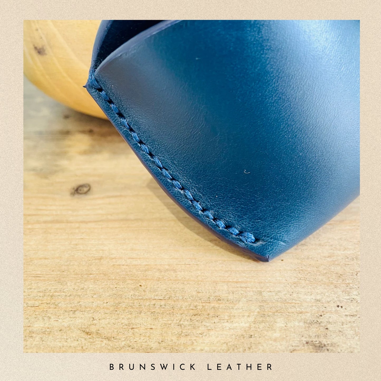 Close-up of a blue leather product with visible stitching on a wooden surface, branded 'Brunswick Leather'.