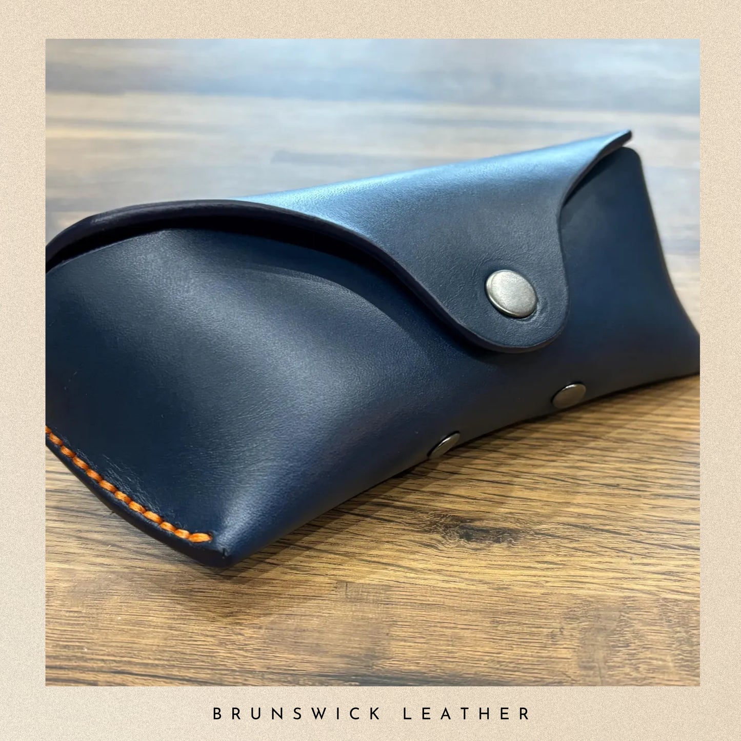 Blue leather case with silver studs on a wooden surface, branded 'Brunswick Leather'.