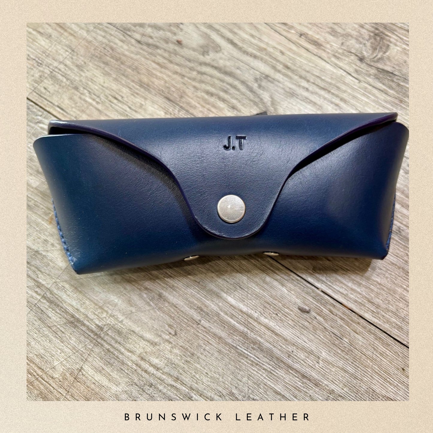 Blue leather case with 'J.T.' initials on a wooden surface, branded 'Brunswick Leather'.