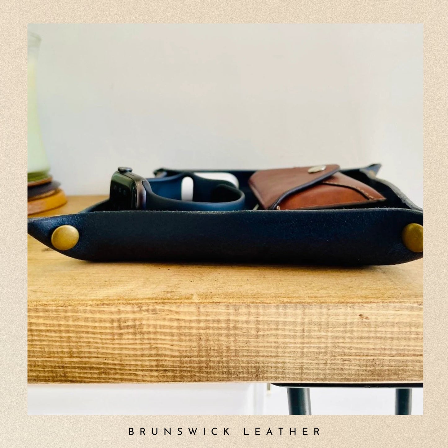 Black leather tray with gold accents on a wooden surface, featuring the brand 'Brunswick Leather'.