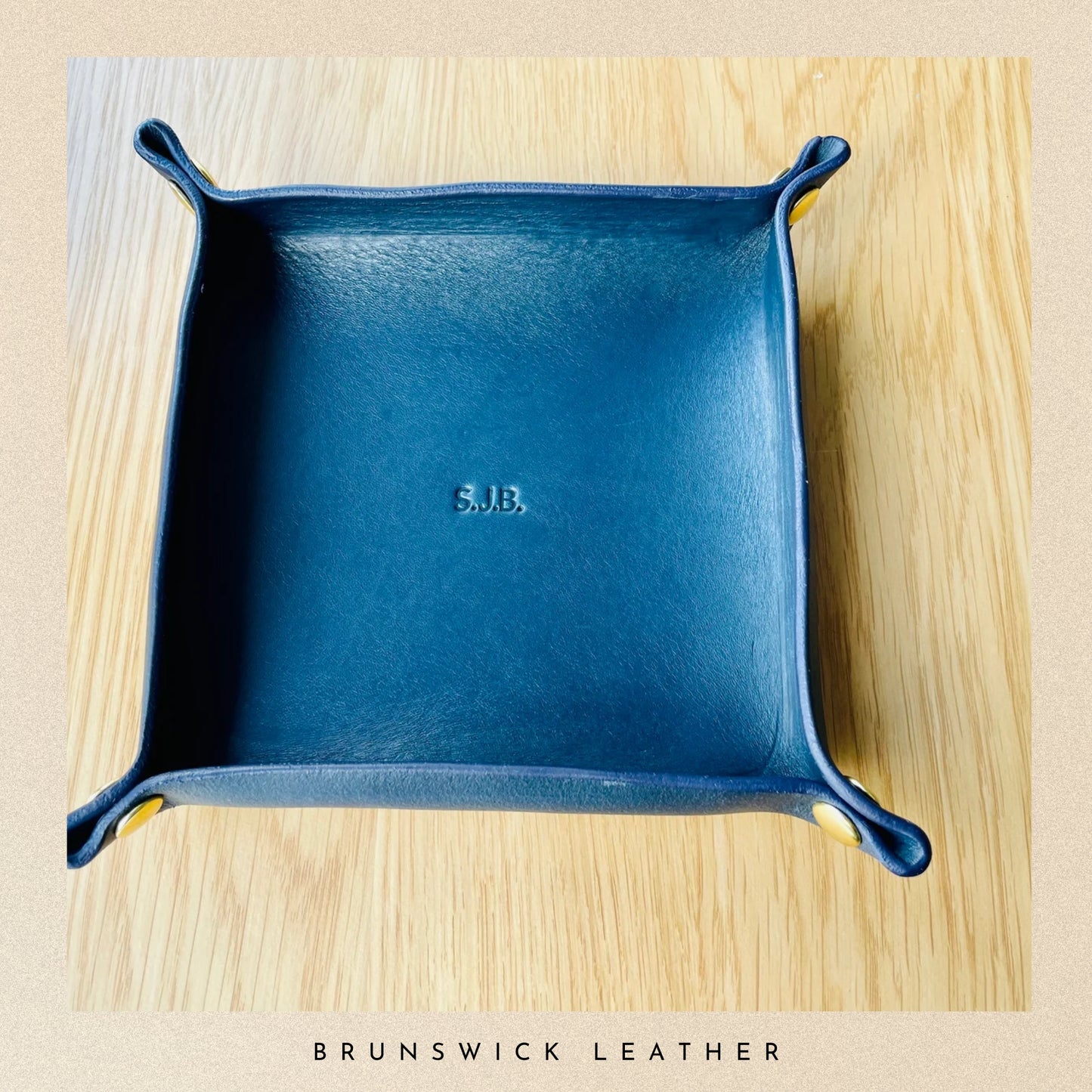 Blue leather tray with 'SJB' initials on a wooden surface, branded 'Brunswick Leather'.