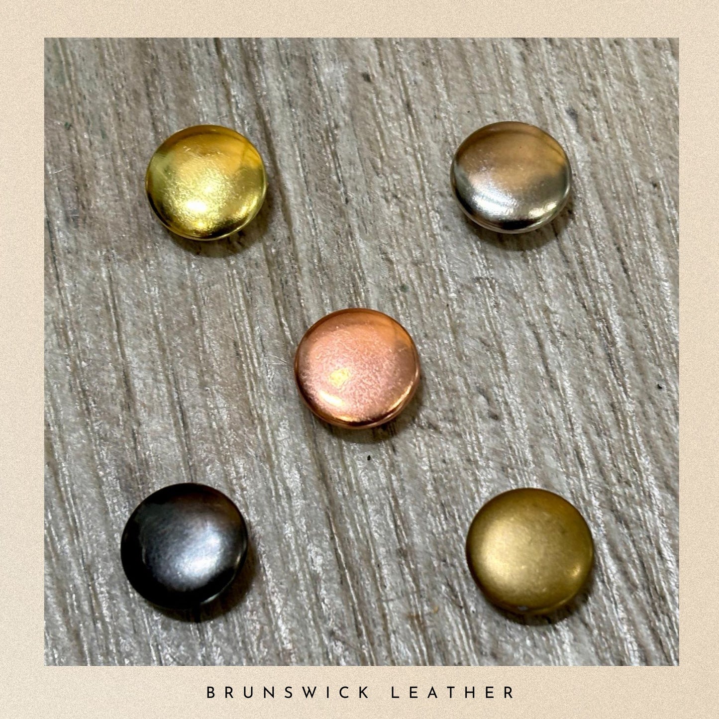 Five metal buttons in gold, silver, bronze, and black on a wooden surface with 'Brunswick Leather' branding.