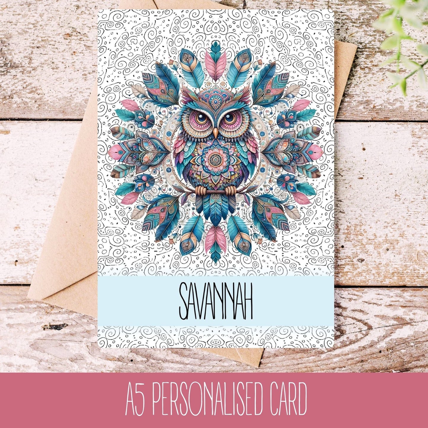 A personalised greeting card with a colorful mandala design shaped like an owl, featuring the name 'SAVANNAH' on it. The card is displayed on a wooden background with a white envelope.