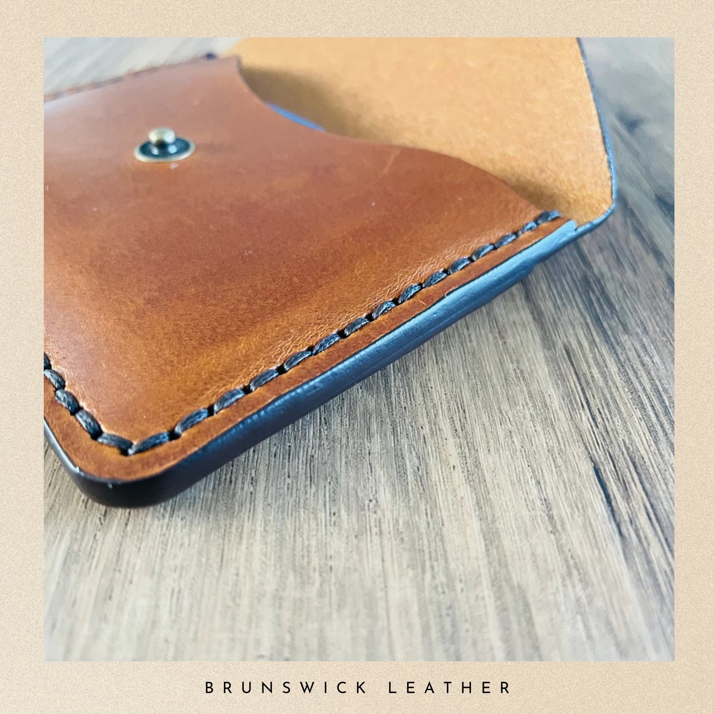 Brown leather wallet with blue stitching on a wooden surface, branded 'Brunswick Leather'.