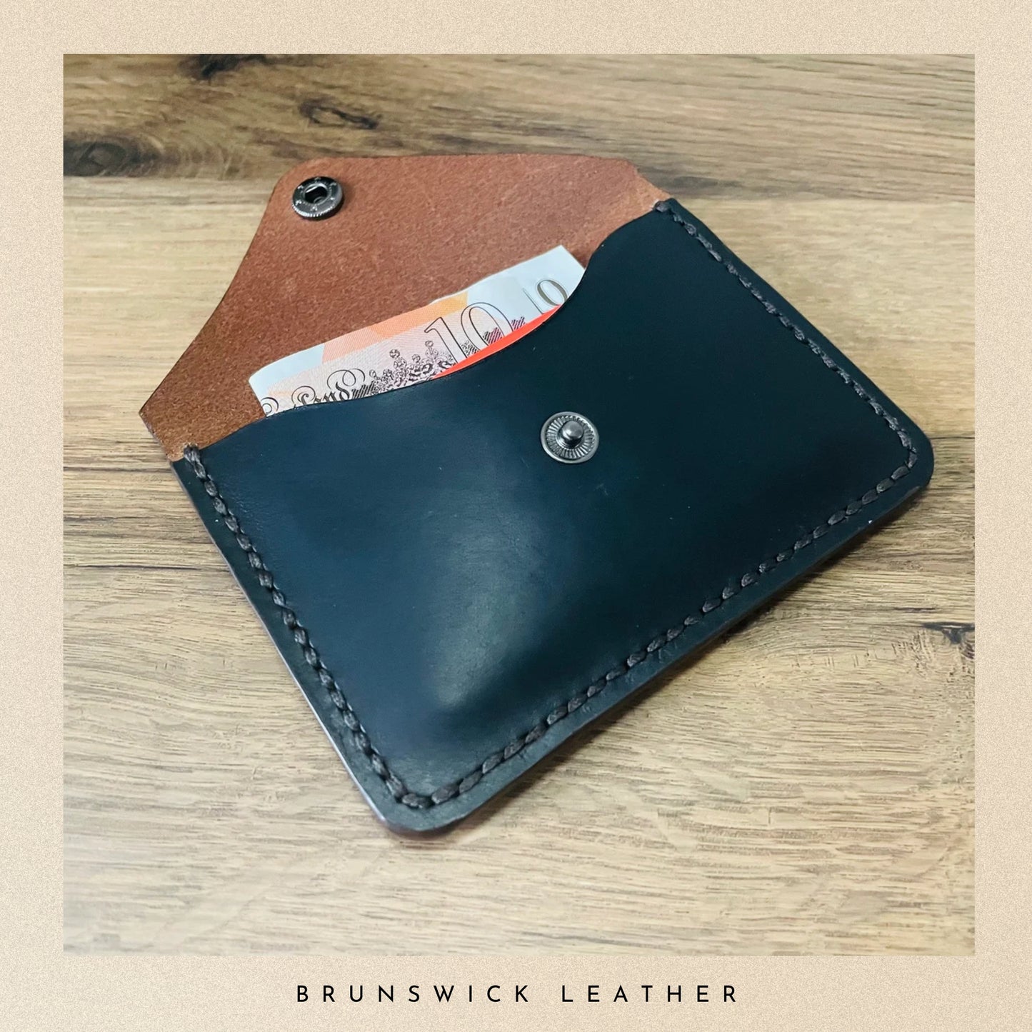 Black leather wallet with brown interior on a wooden surface, branded 'Brunswick Leather'.