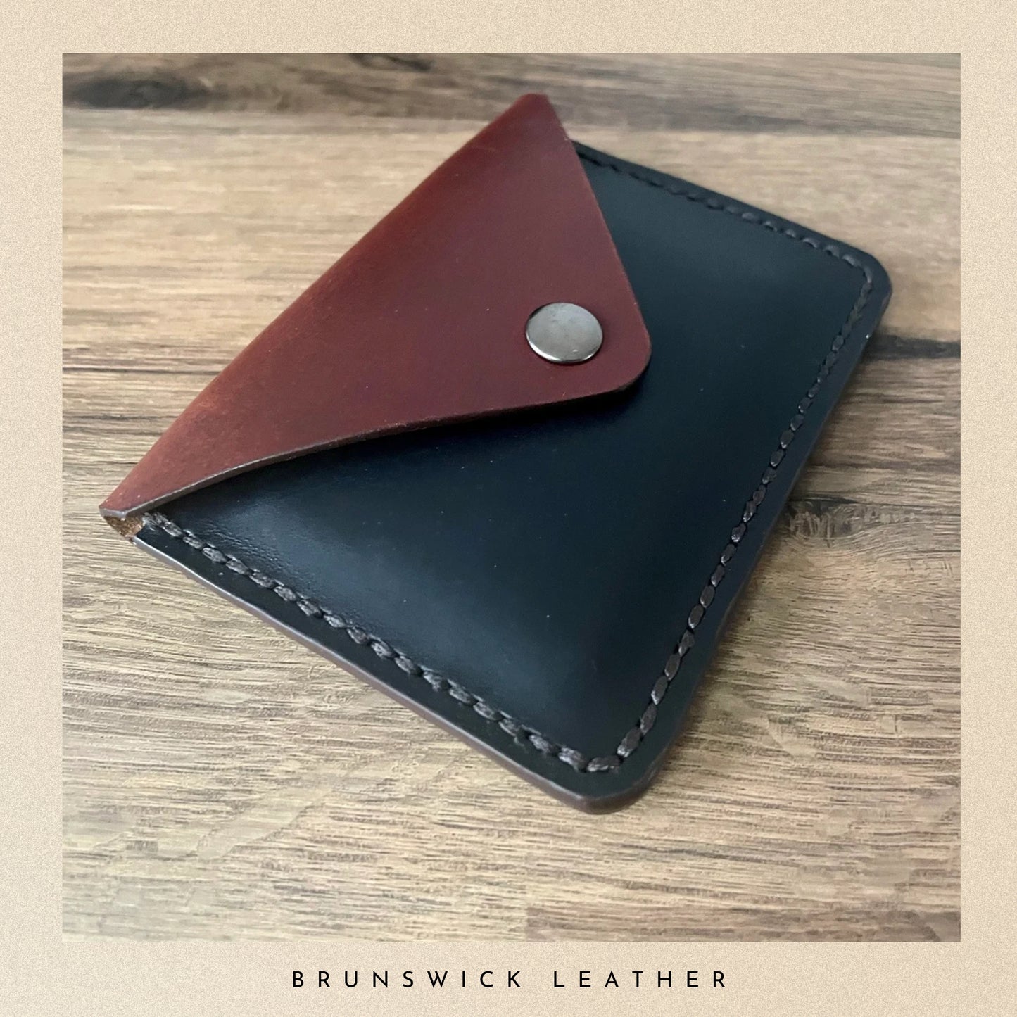 Two-tone leather wallet with brown flap and silver button on a wooden surface, branded 'Brunswick Leather'.
