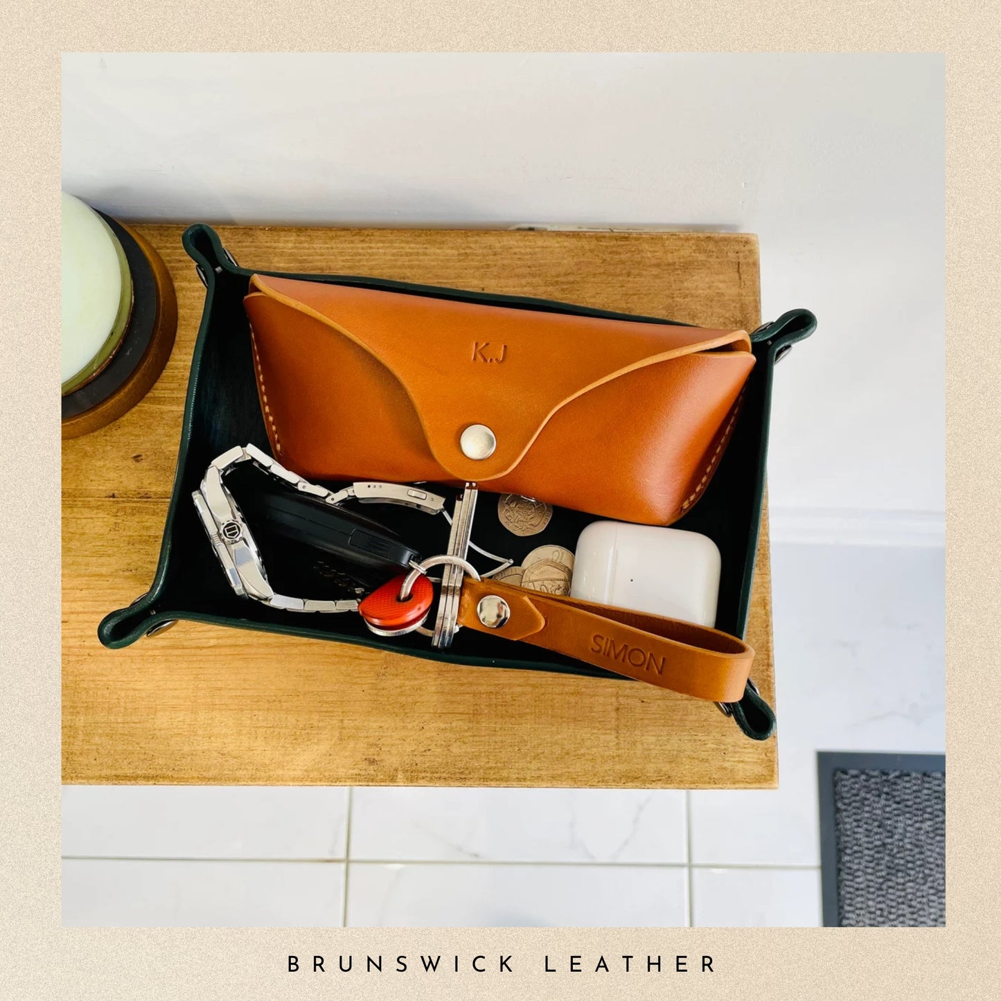 Leather tray with various items on a wooden surface, featuring the brand 'Brunswick Leather'.