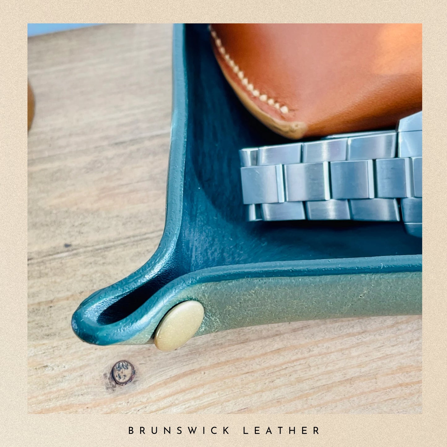 Watch with a blue case and silver band on a wooden surface, branded 'Brunswick Leather'.