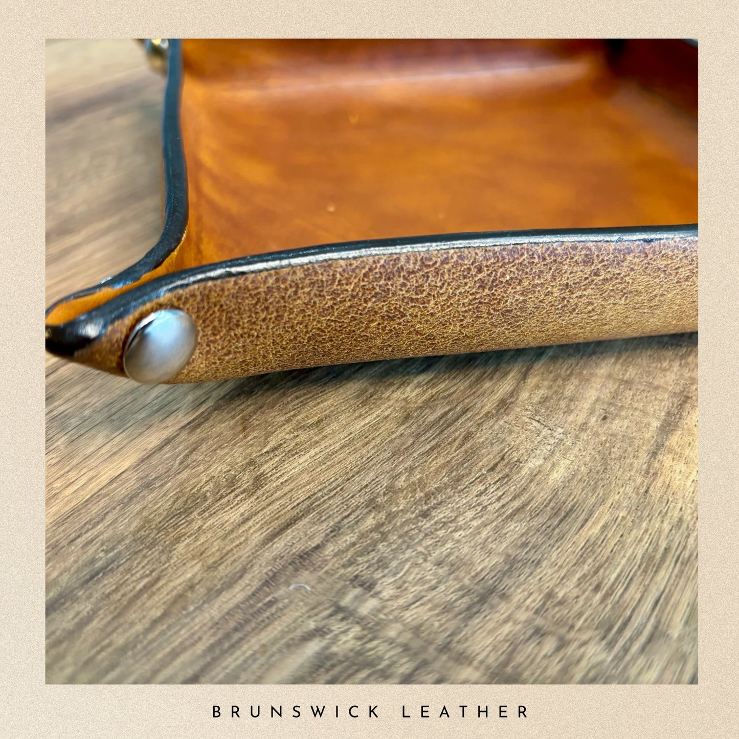 Close-up of a leather product with a metallic accent on a wooden surface, branded 'Brunswick Leather'.