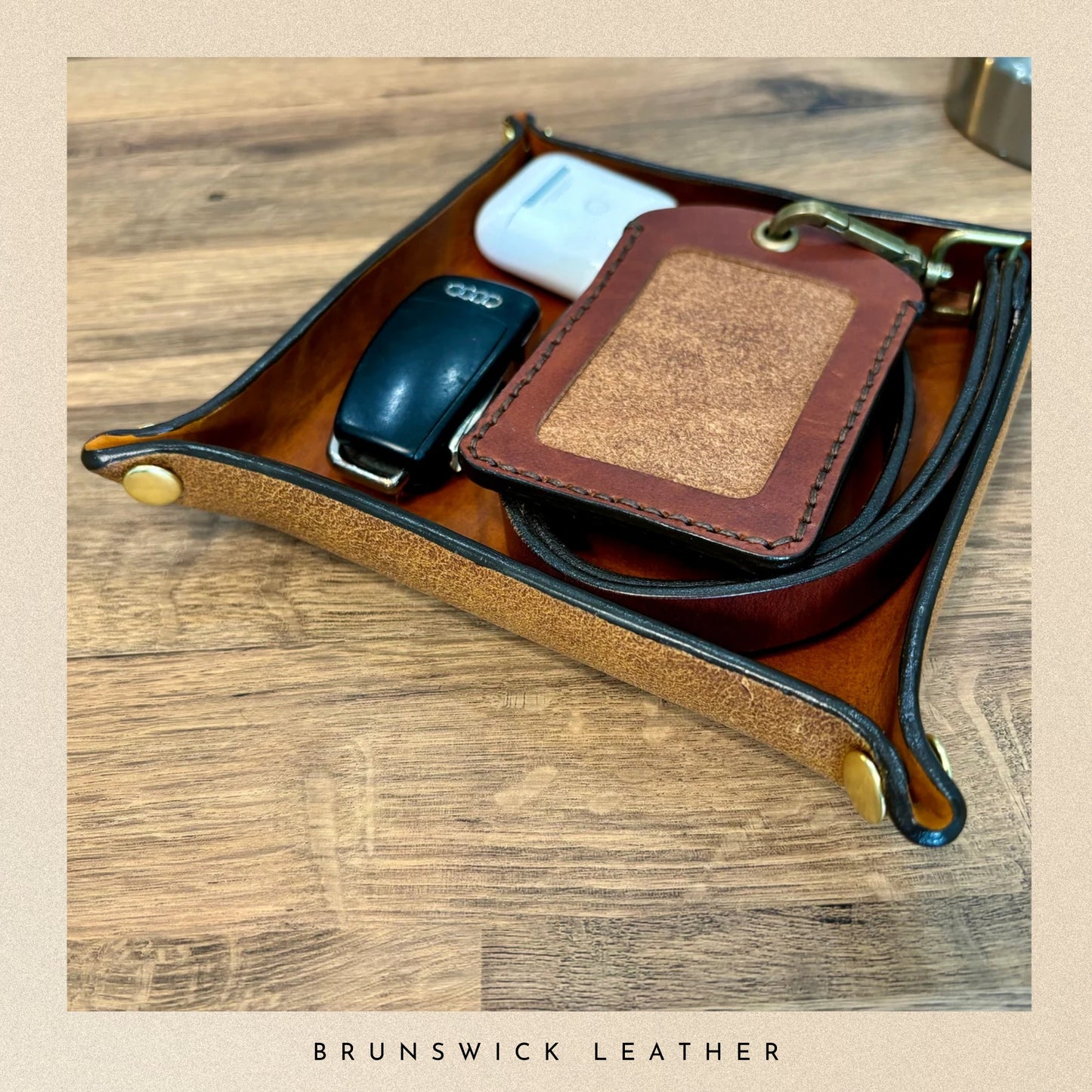 Leather tray with phone, wallet, and keys on a wooden surface, branded 'Brunswick Leather'.